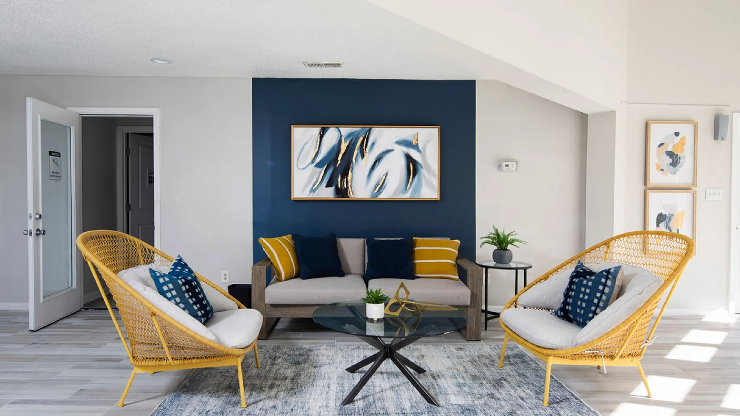 Bright and chic living area featuring modern decor, sunlight streaming through large windows, and stylish rattan chairs.