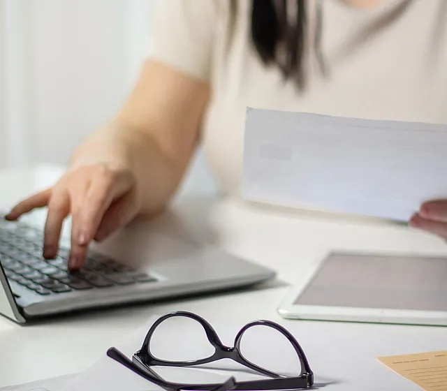 Person multitasking efficiently at a desk with a laptop, tablet, and paperwork, reflecting a productive and organized workspace.