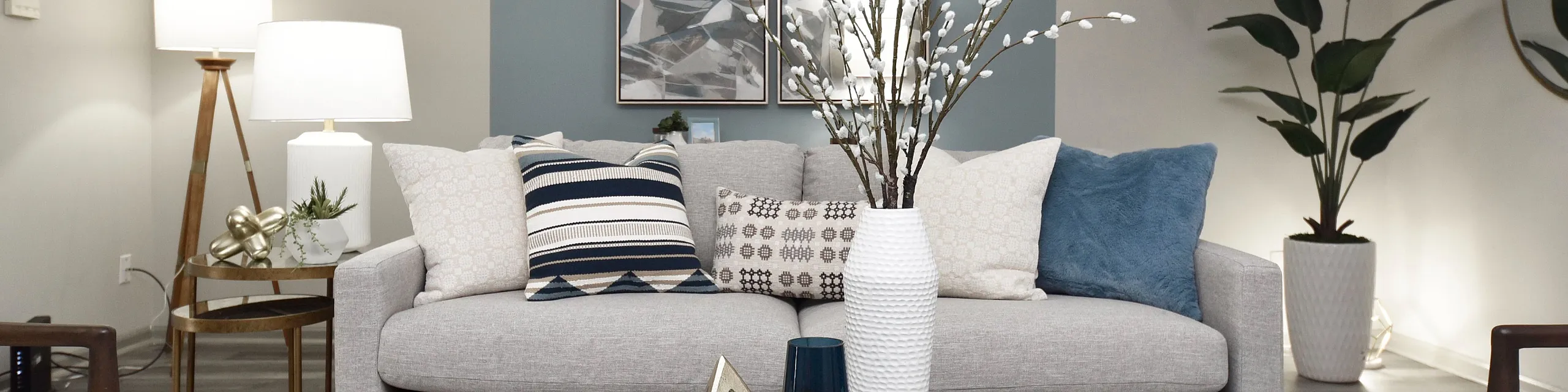 Elegant living room with a modern gray sofa, stylish cushions, and chic decor elements, beautifully lit by contemporary lamps and complemented by green plants.
