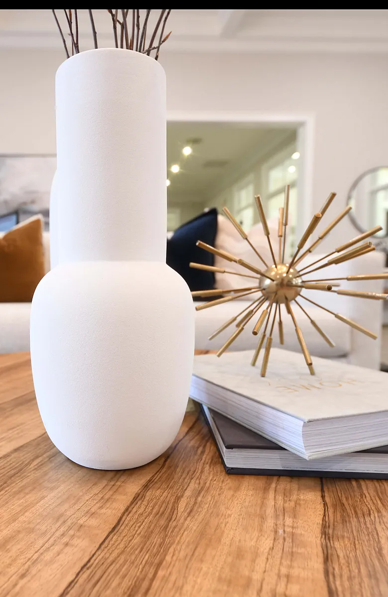 Sophisticated living room with modern decor, featuring a sleek white vase, plush beige sofa, and artistic gold sculpture on a polished wooden table.