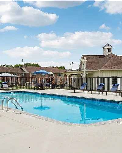 Inviting outdoor pool area with stylish lounge chairs, bright blue umbrellas, and charming brick buildings in the background under a clear sky.