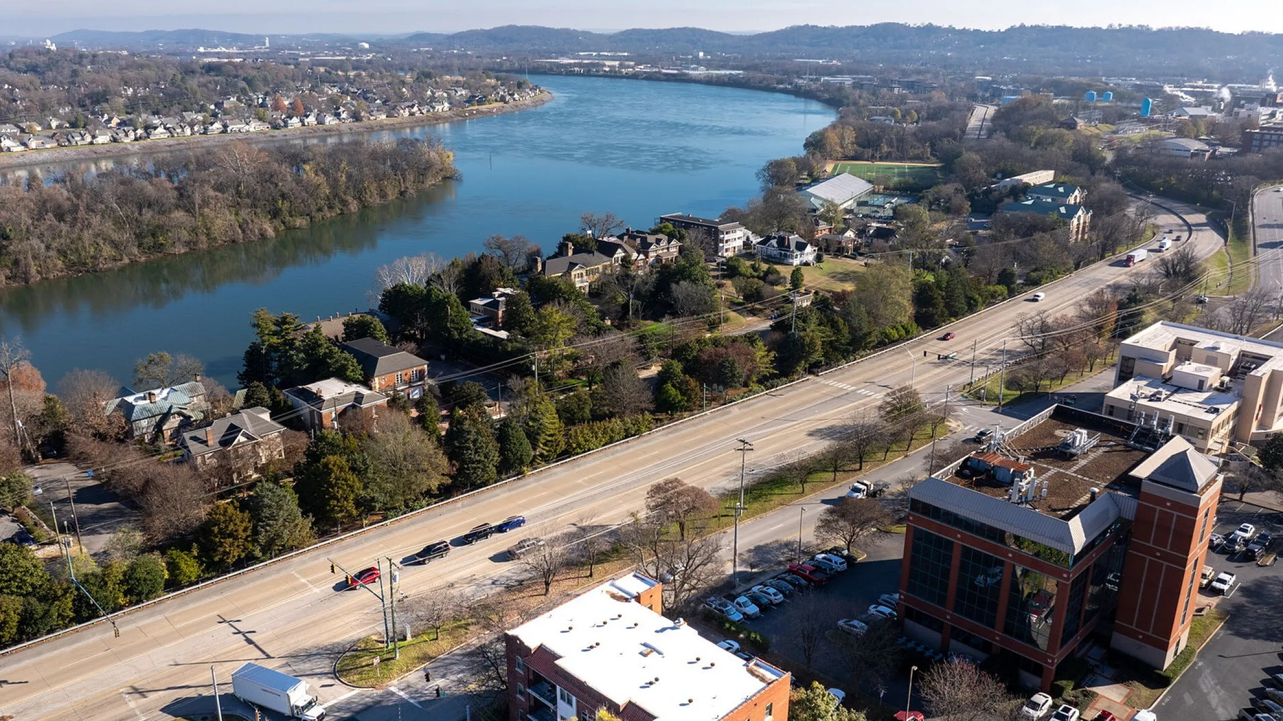 Scenic aerial view of a vibrant urban neighborhood, featuring a serene river, lush greenery, and a bustling roadway, ideal for modern living.
