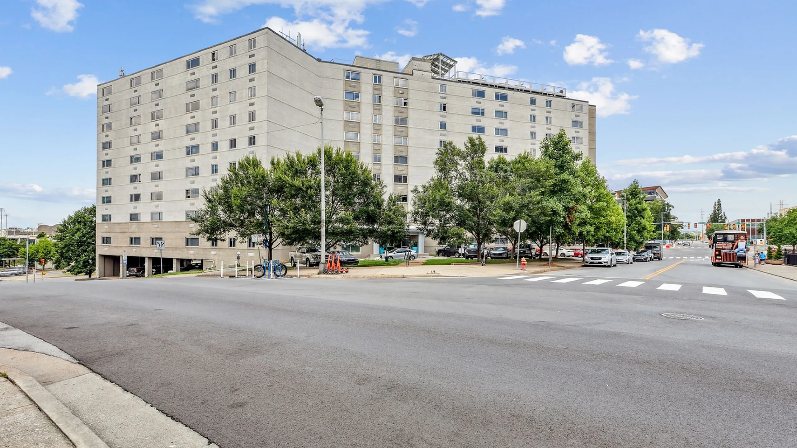 Charming urban apartment building with lush greenery and ample parking, set against a vibrant city backdrop.