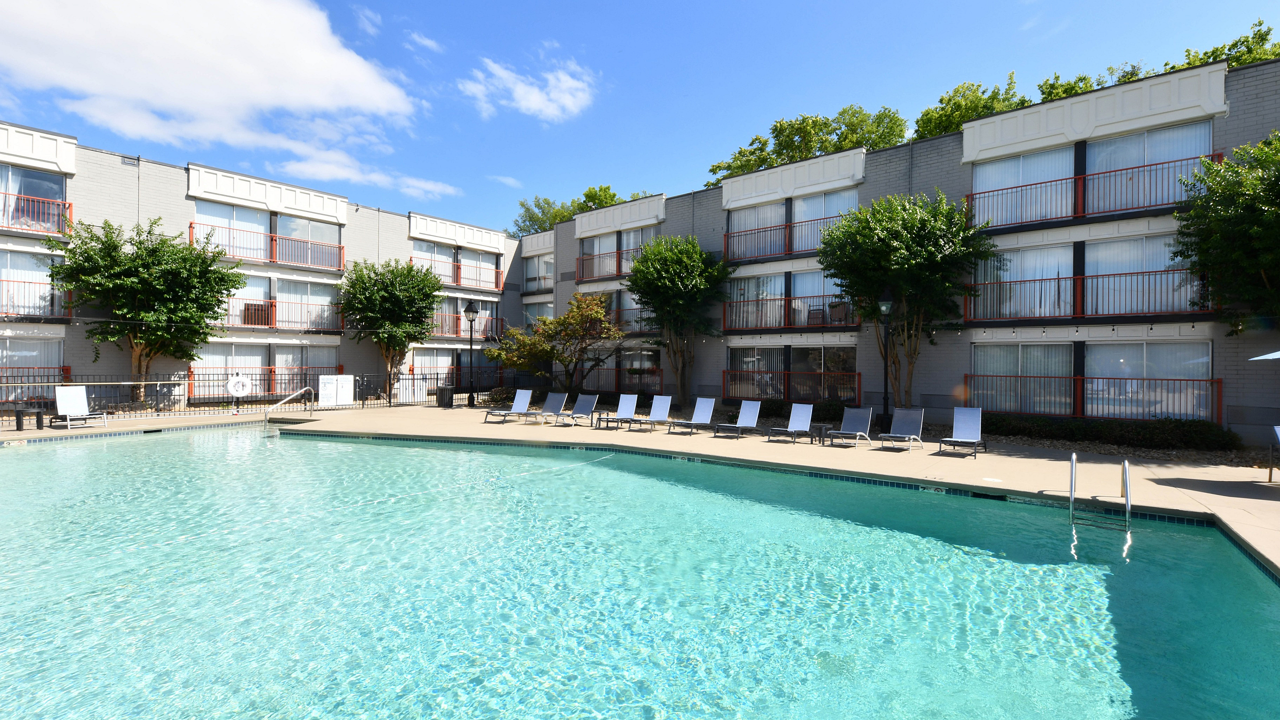 Inviting apartment complex with a sparkling outdoor pool, surrounded by sun loungers and lush greenery, perfect for relaxation and leisure.