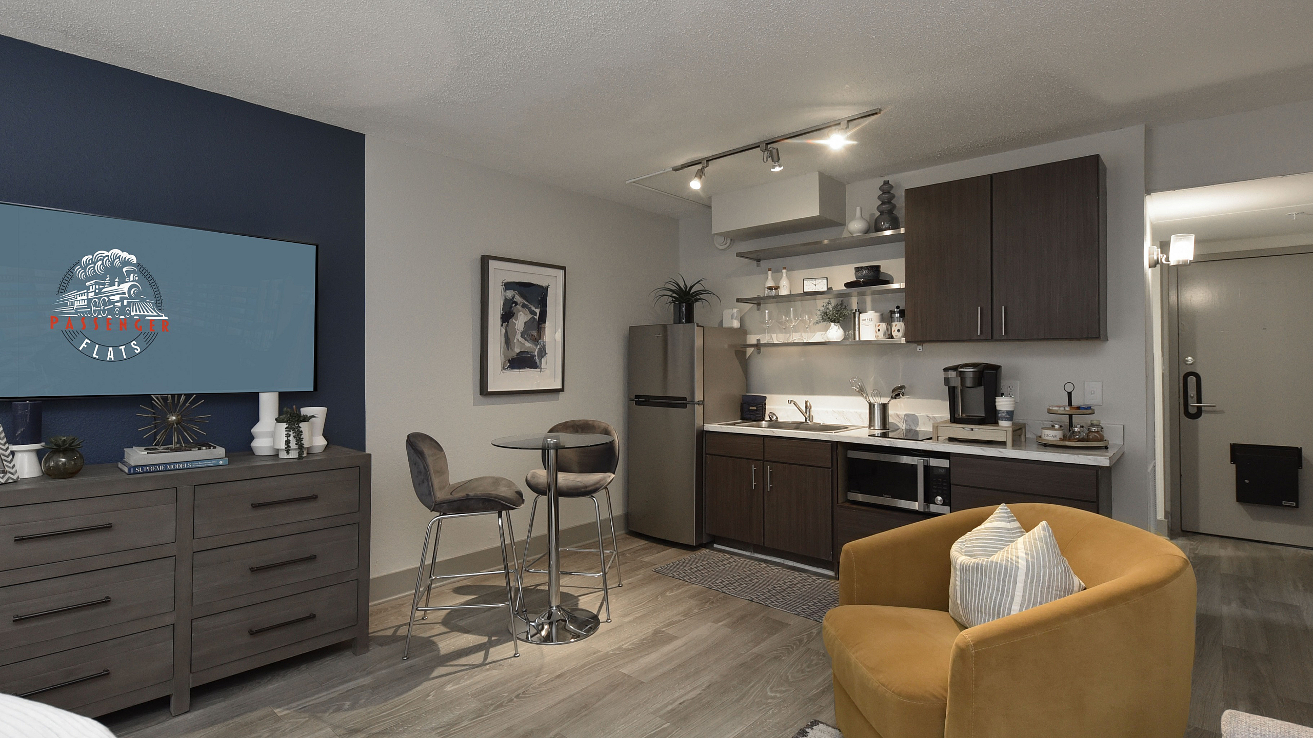 Modern studio apartment featuring a cozy living space with elegant kitchen area, stylish bar stools, and warm lighting.