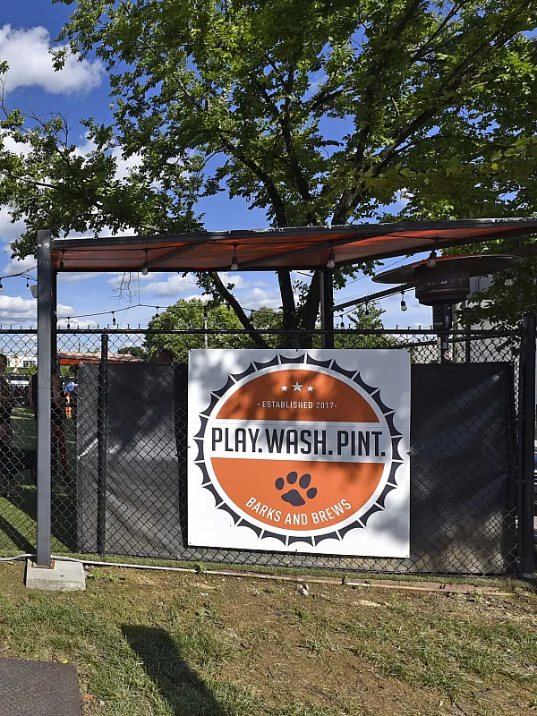 Vibrant outdoor dog park and social space featuring a fun-filled atmosphere with a play area, wash station, and cozy lounging under sunny skies.