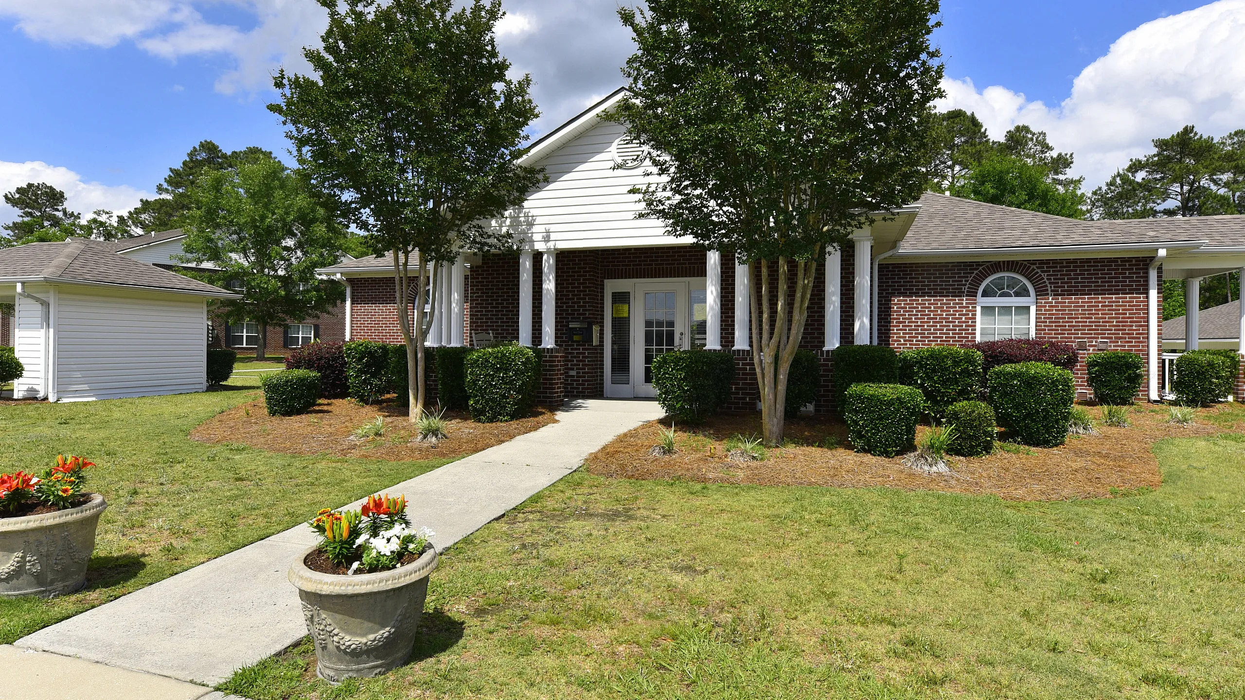 Charming single-story brick townhouse with lush greenery and inviting entrance, perfect for serene living.