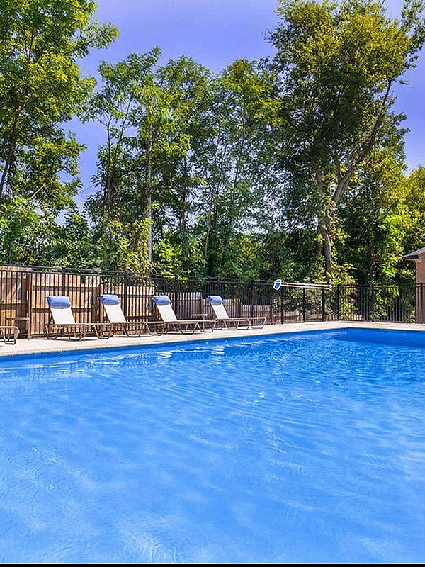 Refreshing outdoor pool area with sunlit lounge chairs, surrounded by lush greenery, perfect for relaxation and leisure.