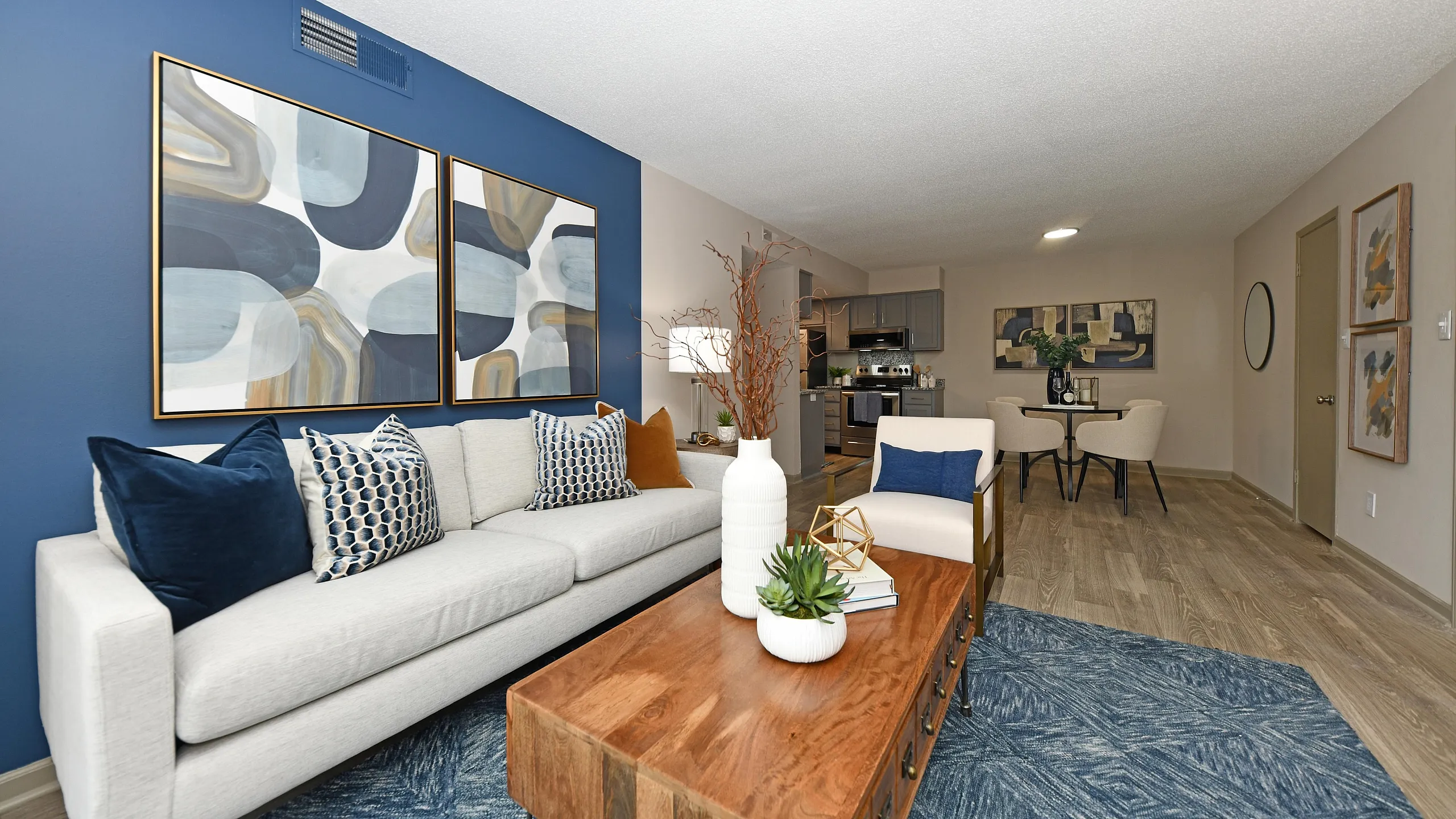 Modern living room with elegant blue accent wall, comfortable beige sofa, stylish abstract art, and open-concept dining area.