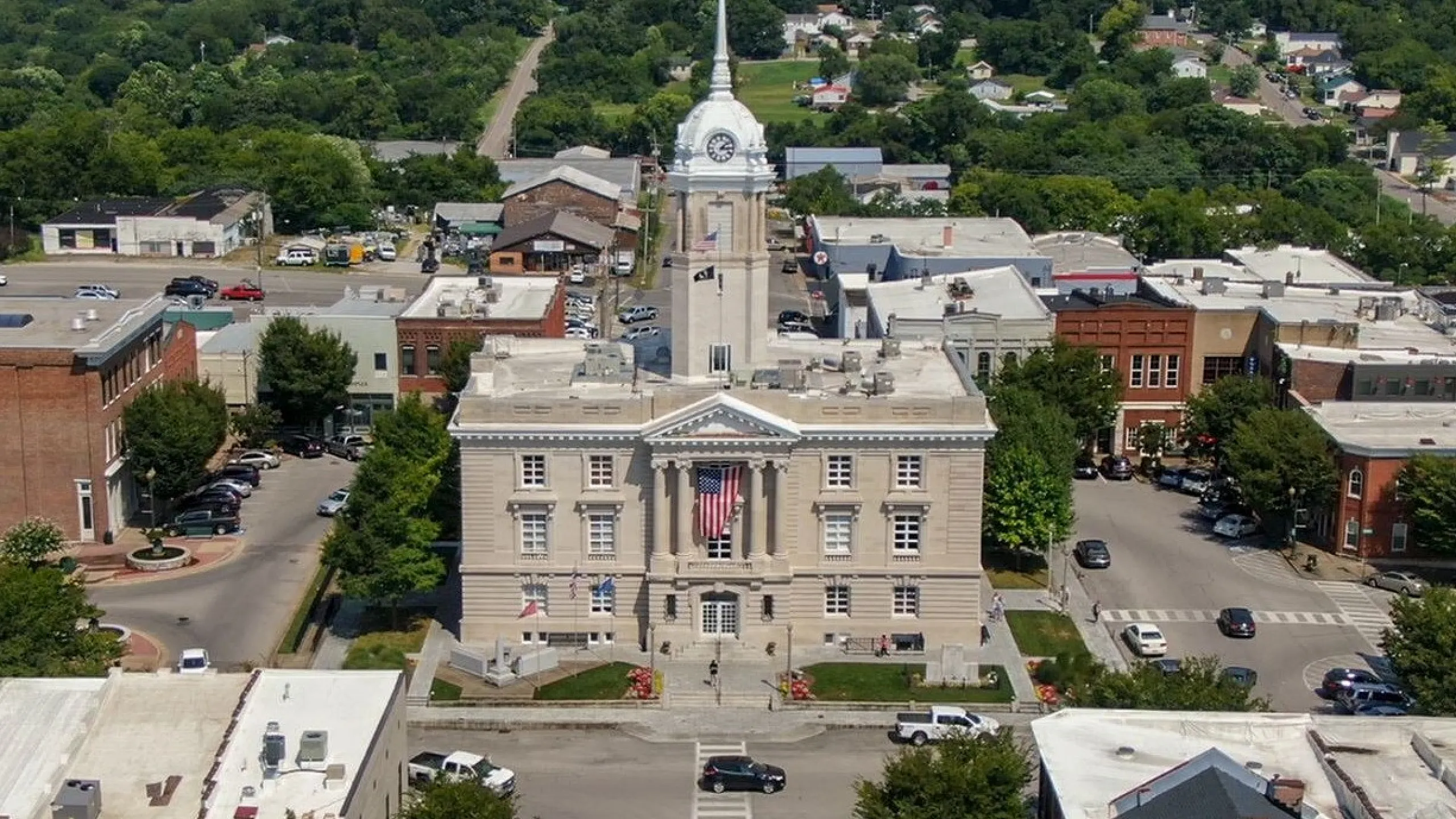 Majestic aerial view of a historic building with a clock tower, surrounded by lush greenery and charming town architecture.