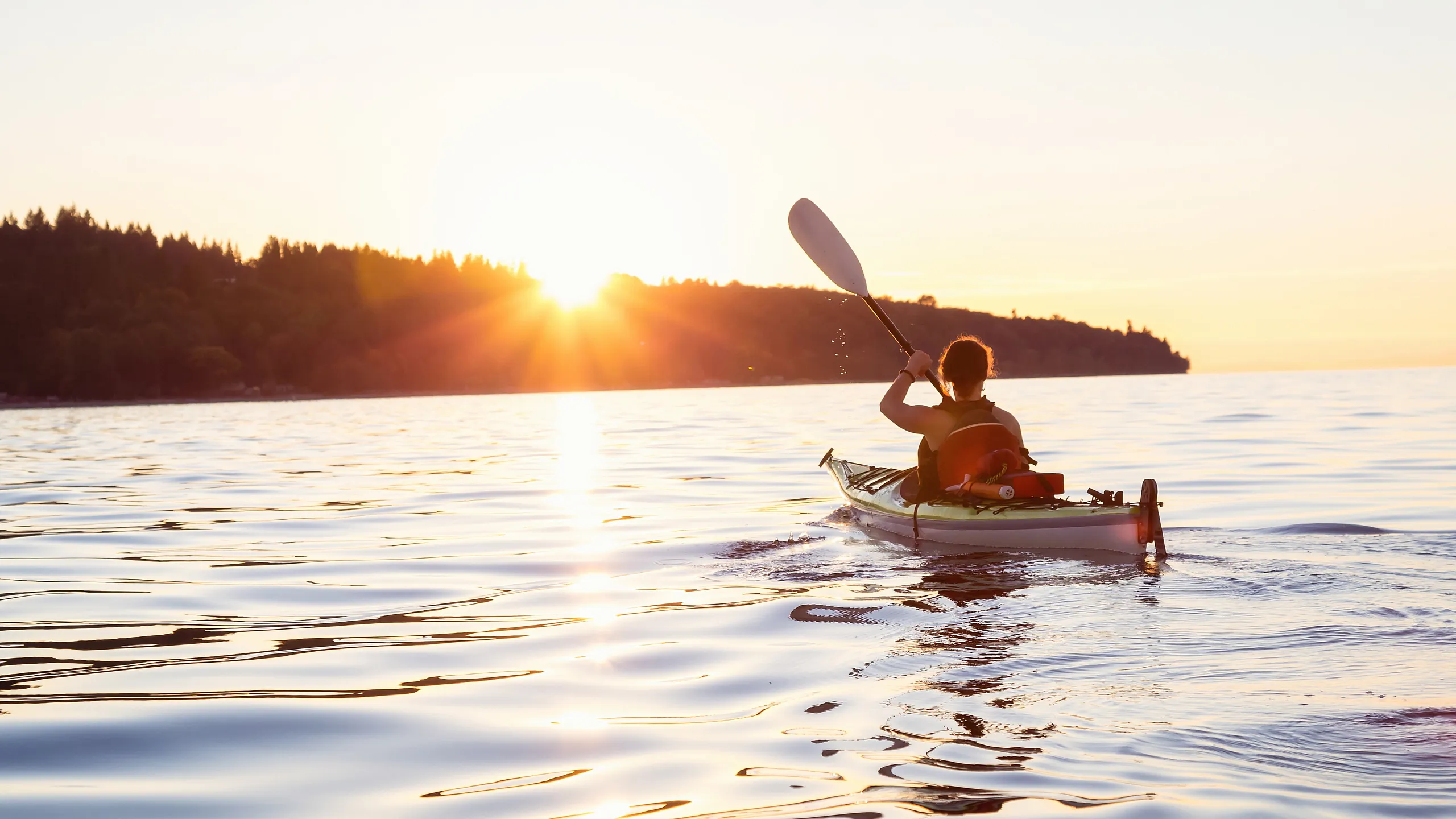 Serene sunset kayaking adventure on tranquil waters, with golden sunlight glistening on the lake.