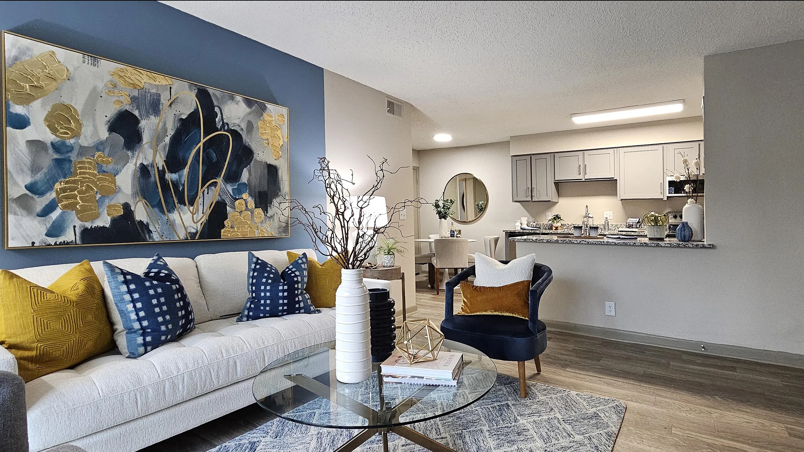 Modern open-concept living room with stylish decor, vivid artwork, and a spacious kitchen area. Cozy seating and elegant lighting enhance the inviting ambiance.