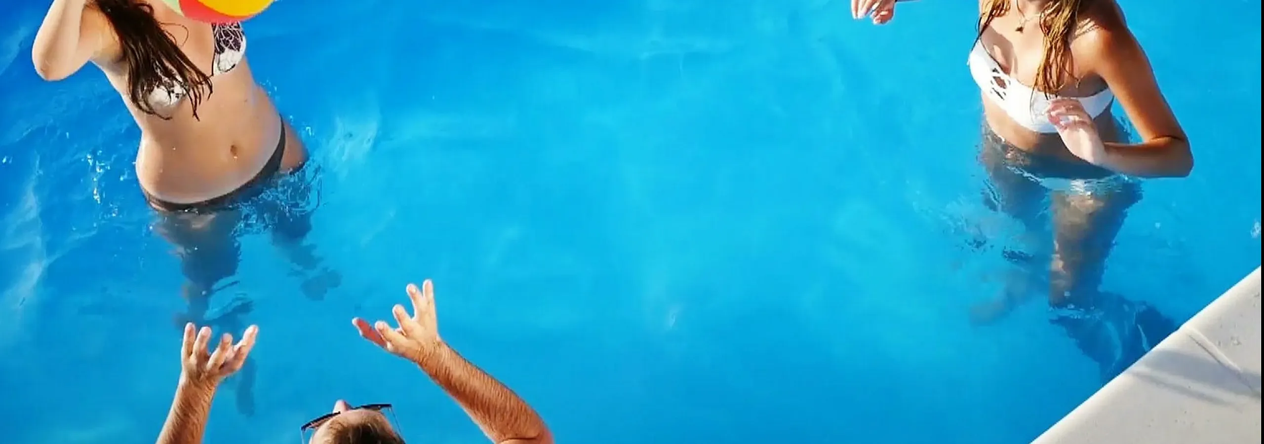 Vibrant pool scene with friends enjoying a sunny day, tossing a colorful beach ball in crystal-clear water.