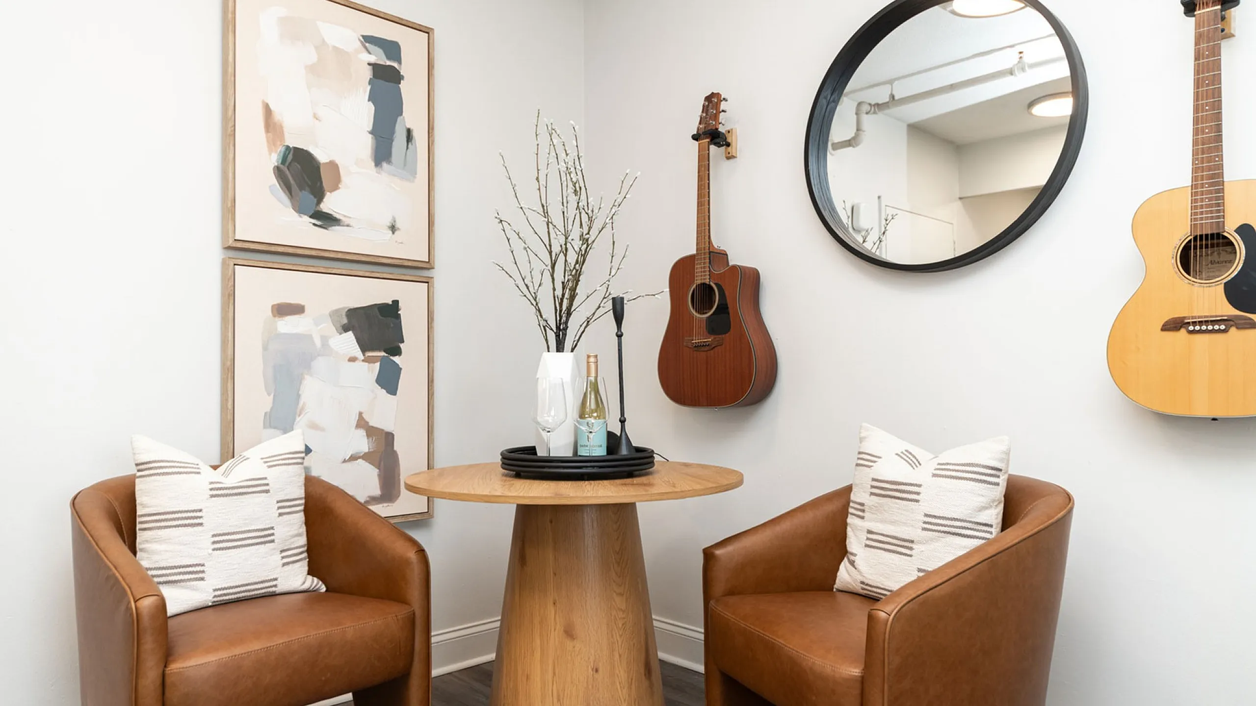 Chic apartment corner with modern abstract art, acoustic guitars, and cozy seating with leather chairs around a stylish wooden table.