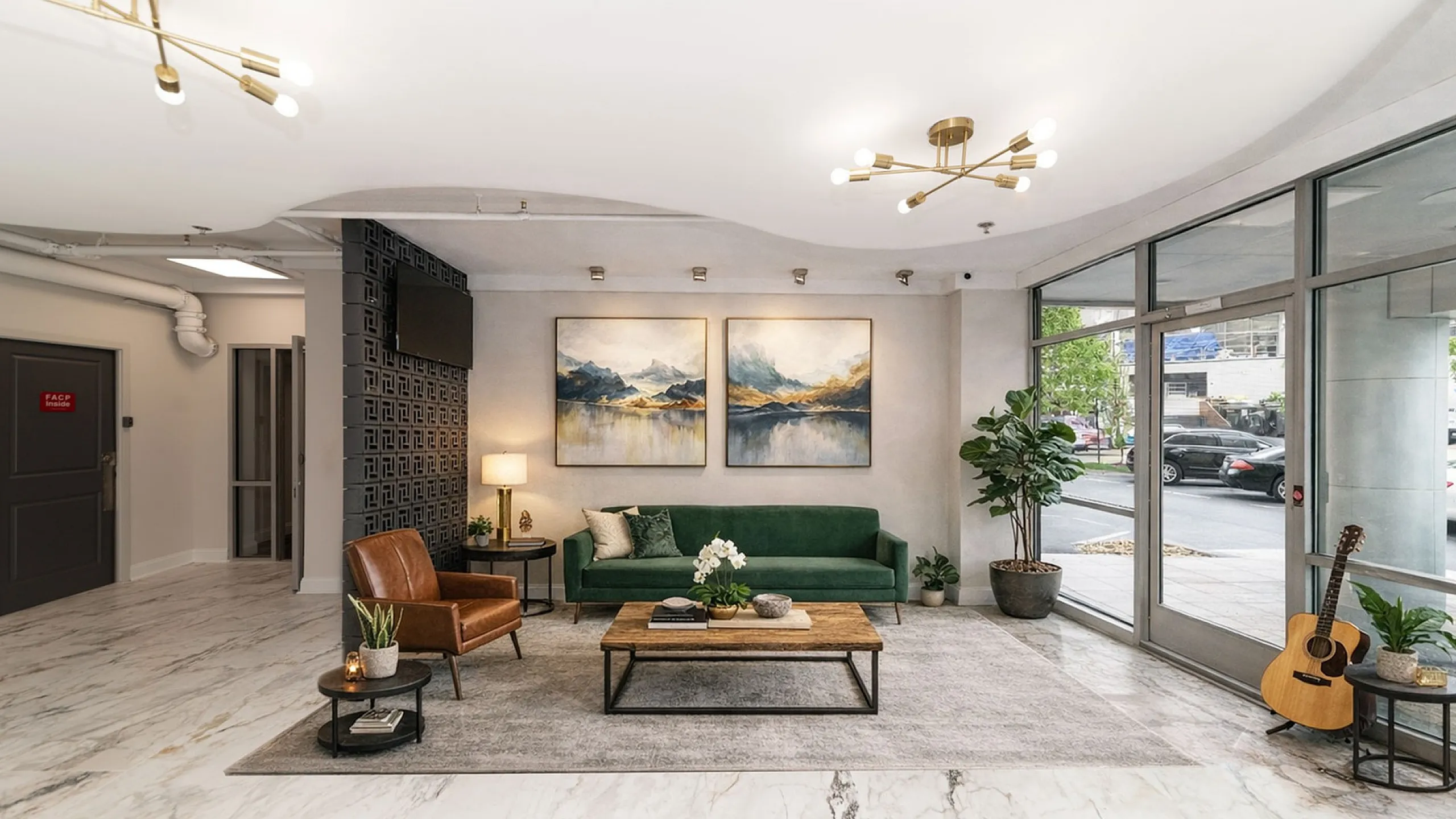 Modern lobby with elegant decor, featuring a green velvet sofa, leather chair, stylish artworks, and a sleek marble floor.
