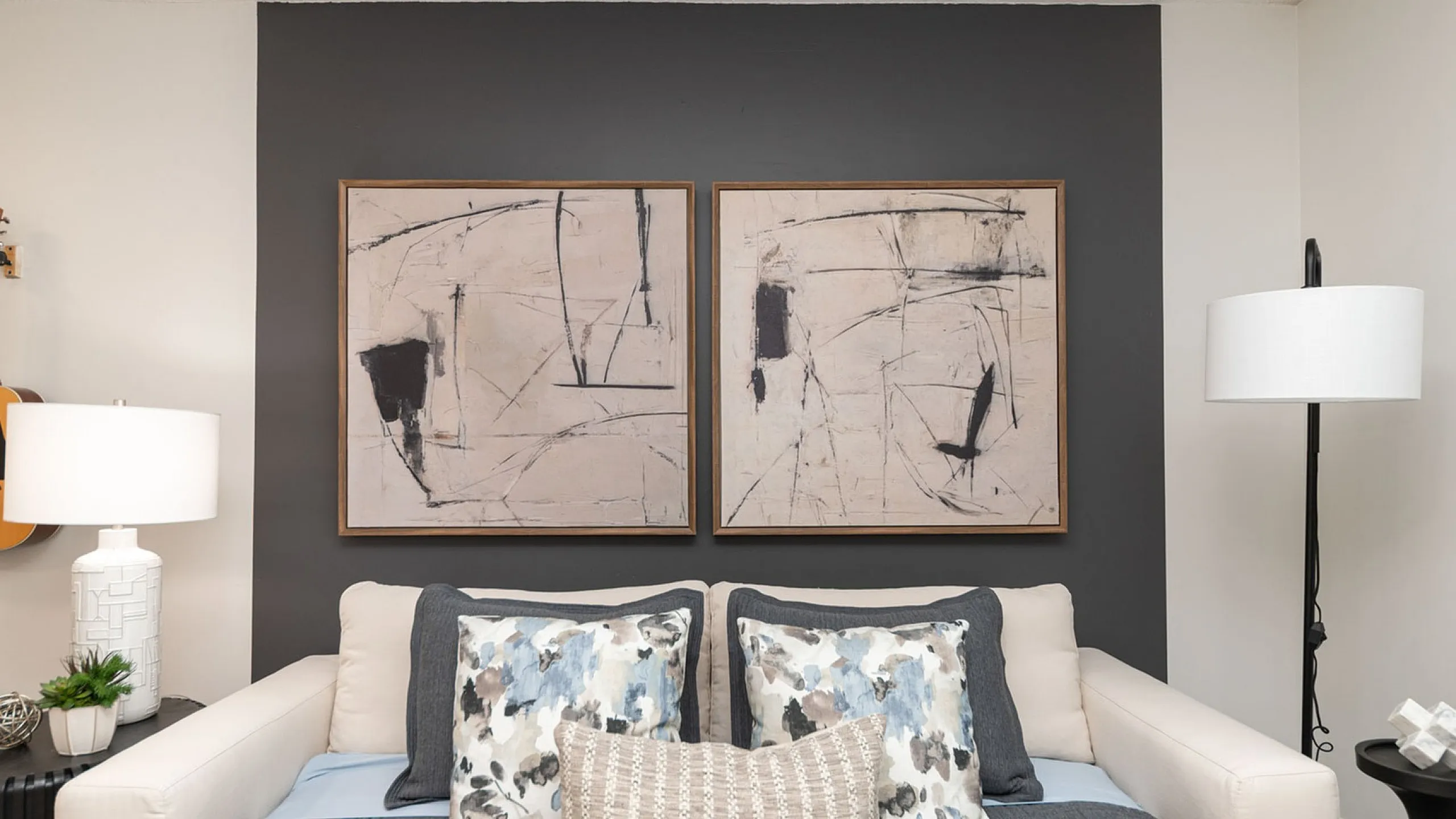 Elegant bedroom with modern abstract art, neutral tones, and cozy pillows, featuring a stylish corner with a guitar and contemporary lighting.