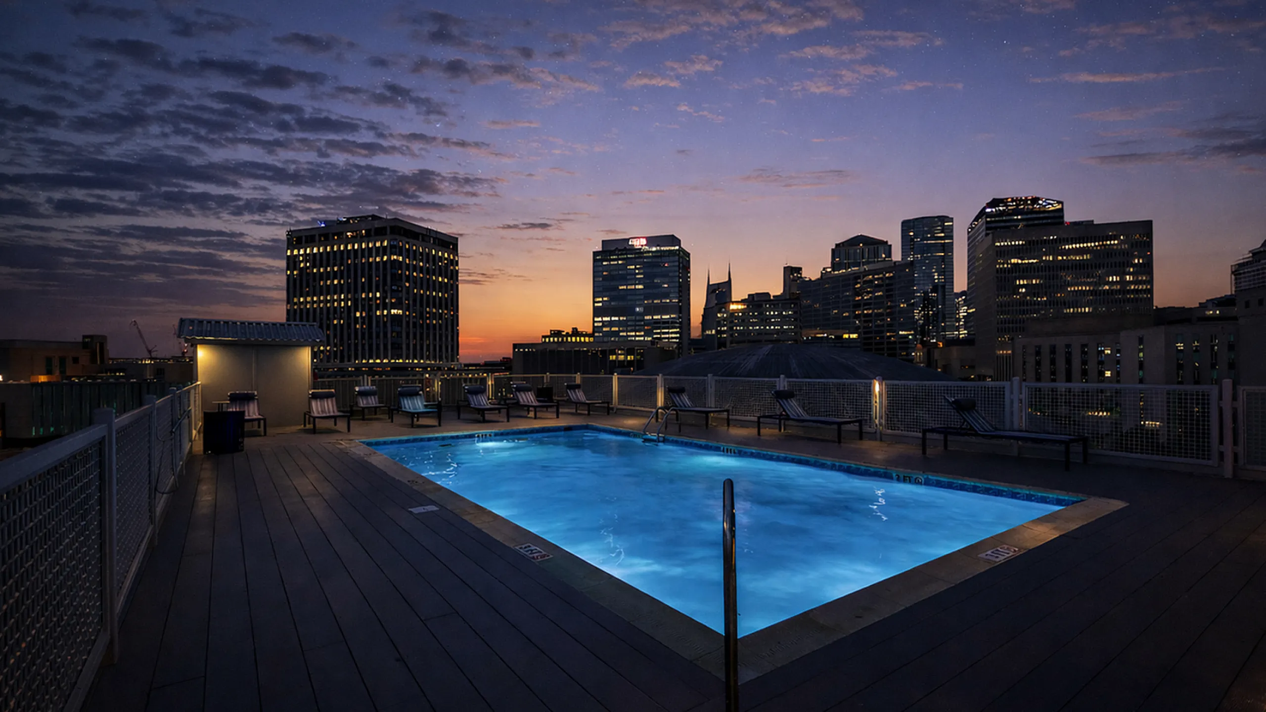 Stunning rooftop pool with breathtaking city skyline views at sunset, offering a perfect urban oasis.