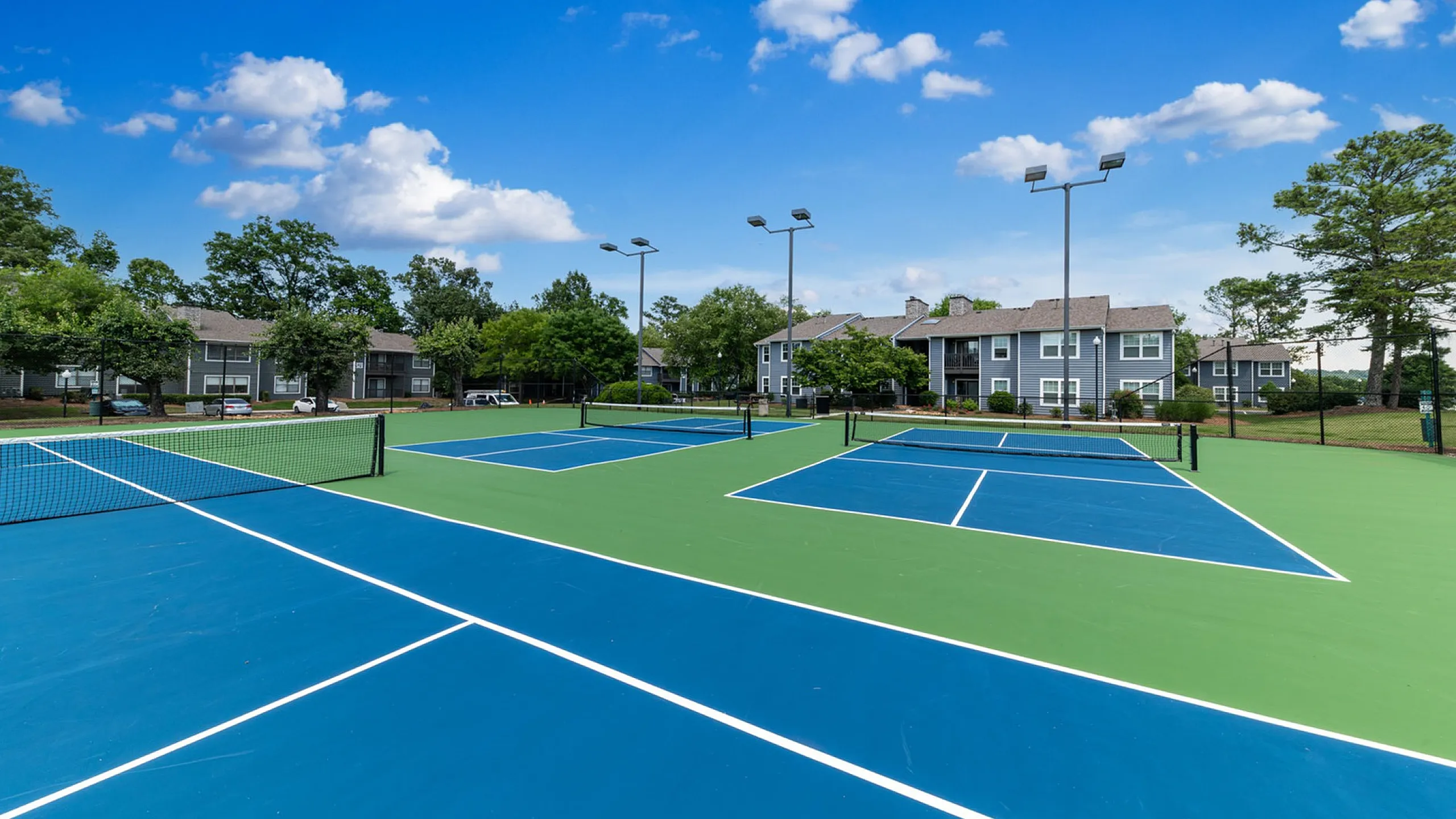 Luxurious apartment community featuring pristine tennis courts surrounded by lush greenery and charming residential buildings.