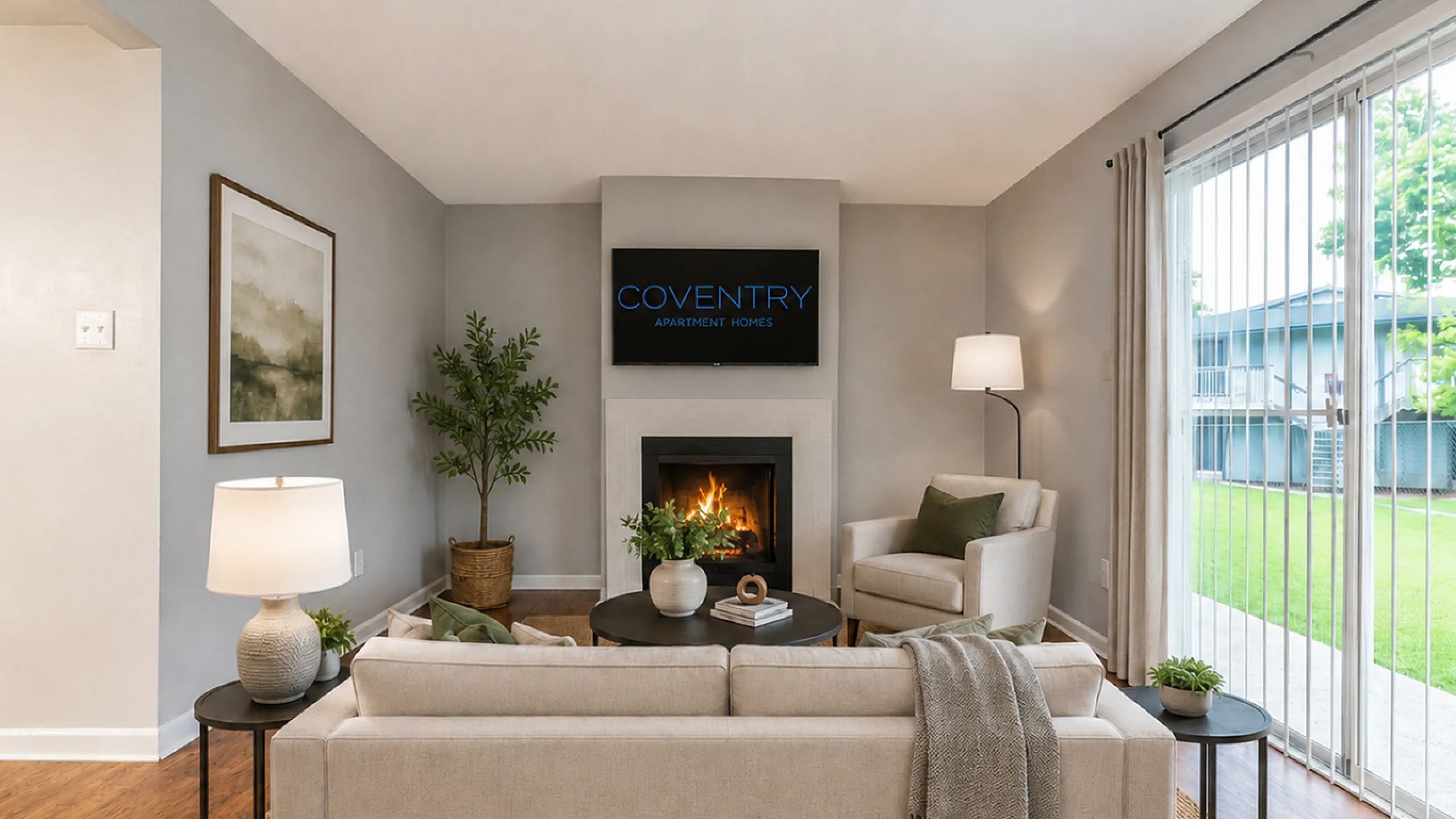 Cozy and stylish living room with contemporary decor, featuring a warm fireplace, elegant furniture, and a view of the lush outdoor garden at Coventry Apartment Homes.