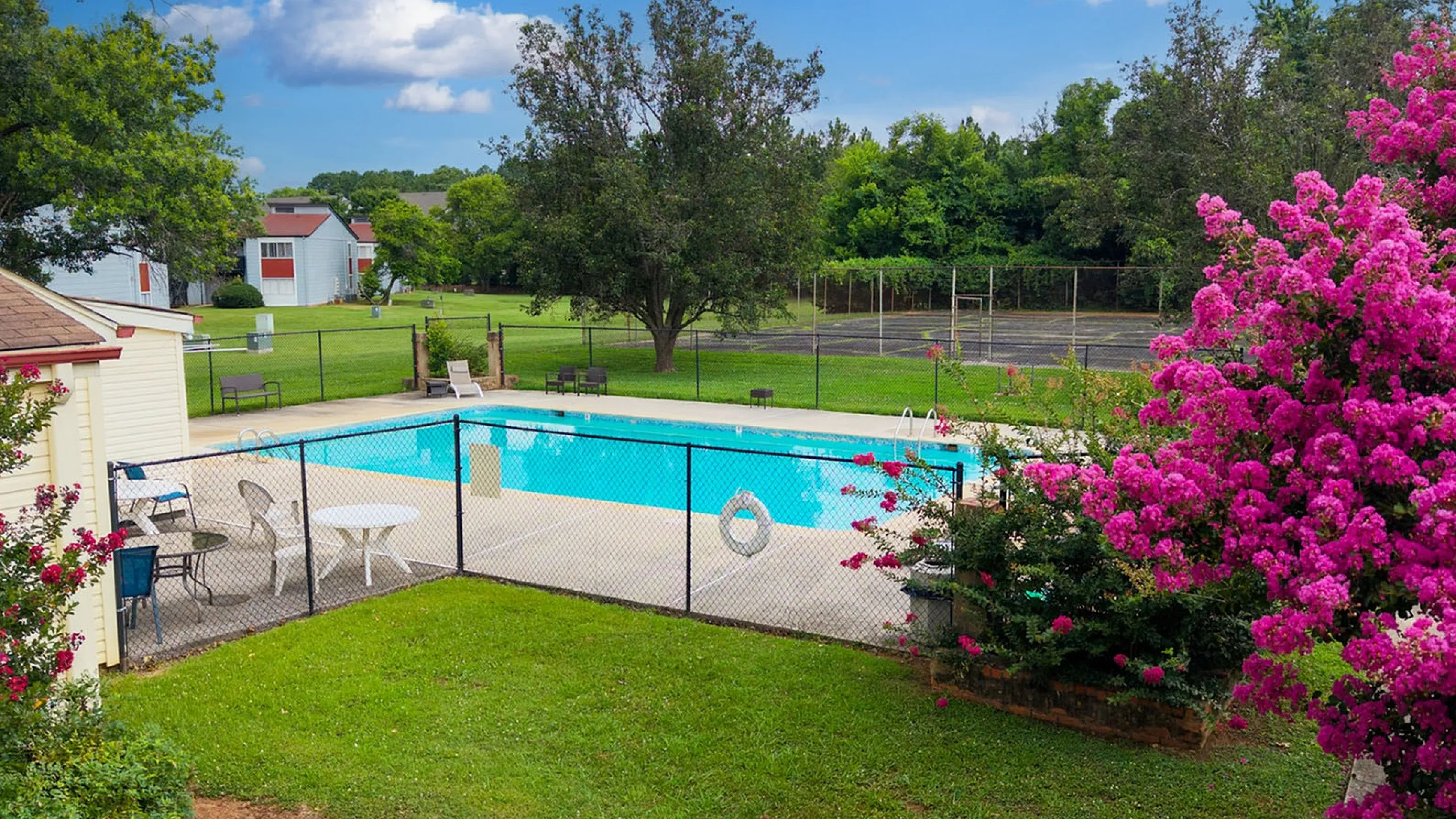Idyllic community pool area with vibrant pink flowers, lush greenery, and clear blue skies.