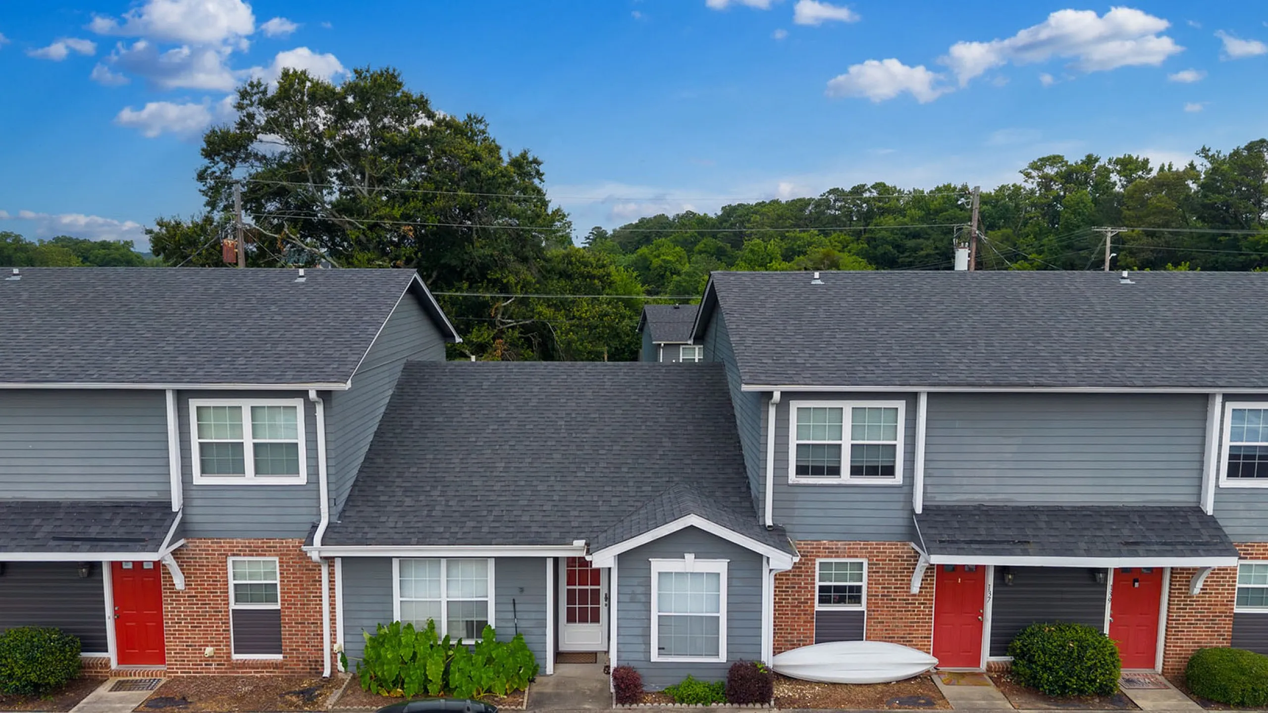 Charming townhouses with brick and siding facade, featuring red doors and picturesque greenery, against a serene blue sky.
