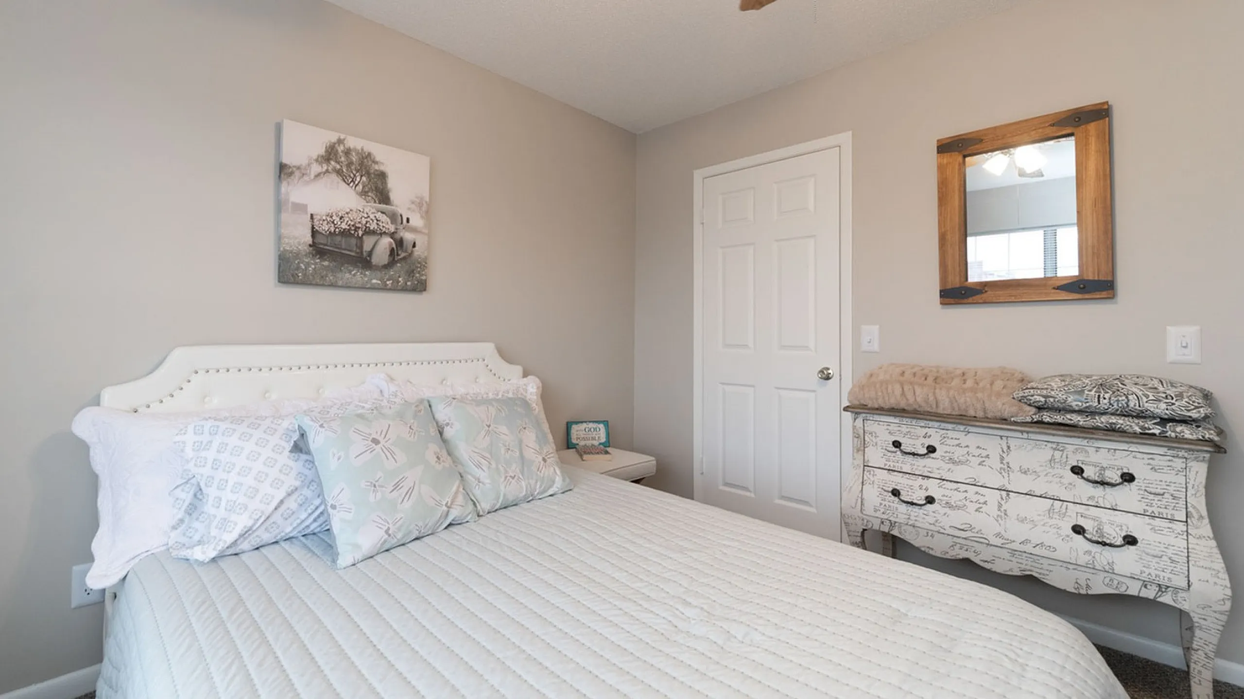 Charming bedroom with elegant decor, featuring a cozy bed, stylish throw pillows, and a vintage dresser under warm lighting.