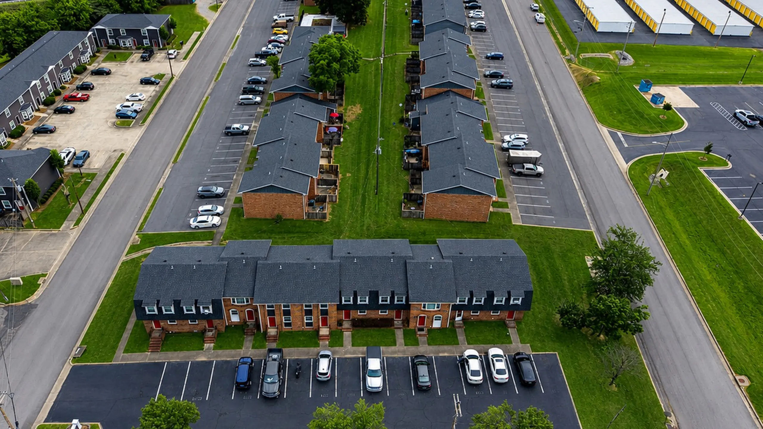 Aerial view of a charming apartment complex featuring modern townhouses with lush green surroundings, ample parking, and convenient road access.