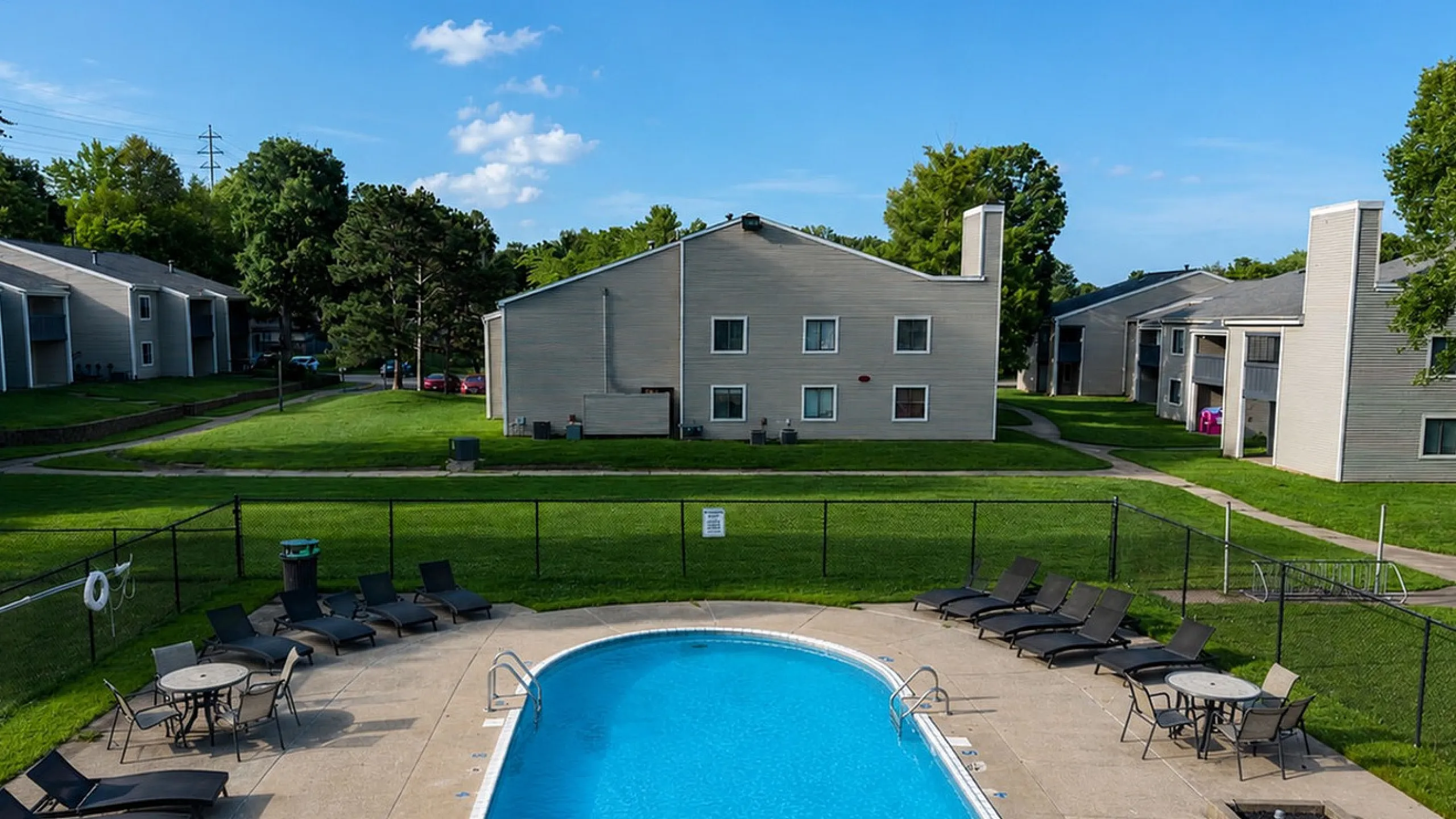 Charming apartment complex with inviting outdoor pool, lush green lawns, and sleek lounge chairs, perfect for relaxation.