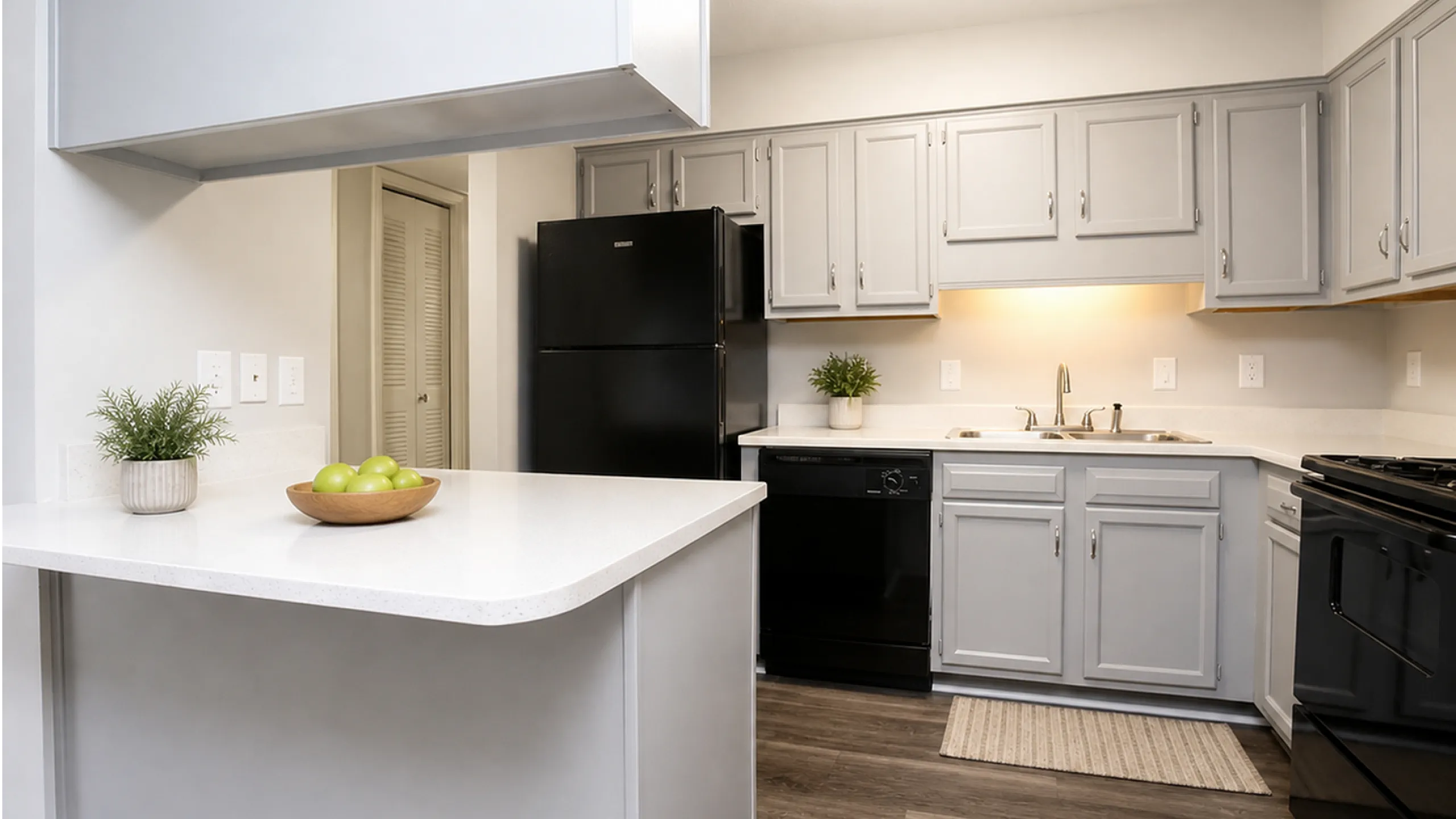 Modern kitchen with sleek gray cabinets, black appliances, and elegant countertop featuring a bowl of green apples.