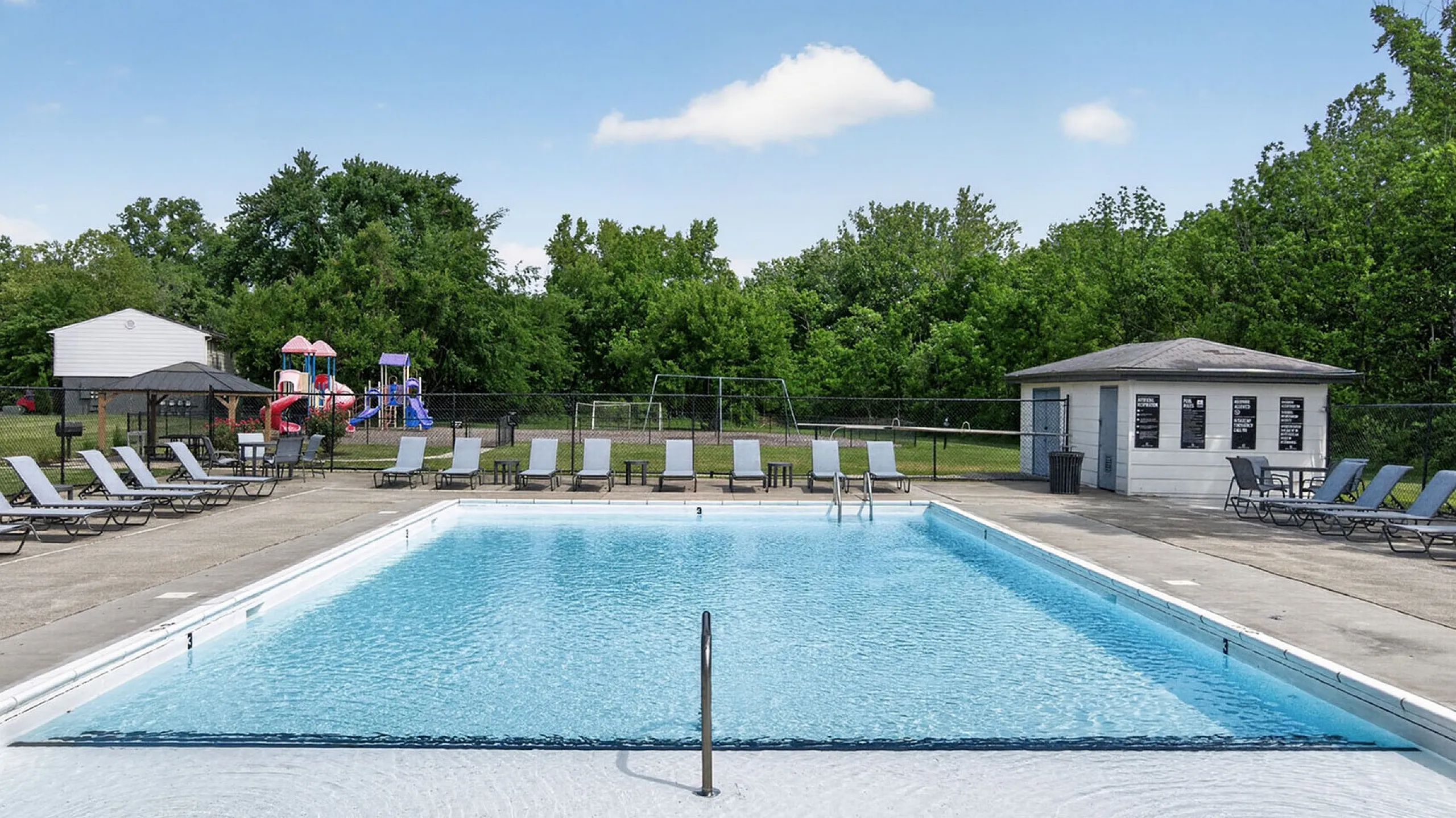 Inviting outdoor pool surrounded by lush greenery and modern lounge chairs, perfect for relaxation and family fun in a serene setting.
