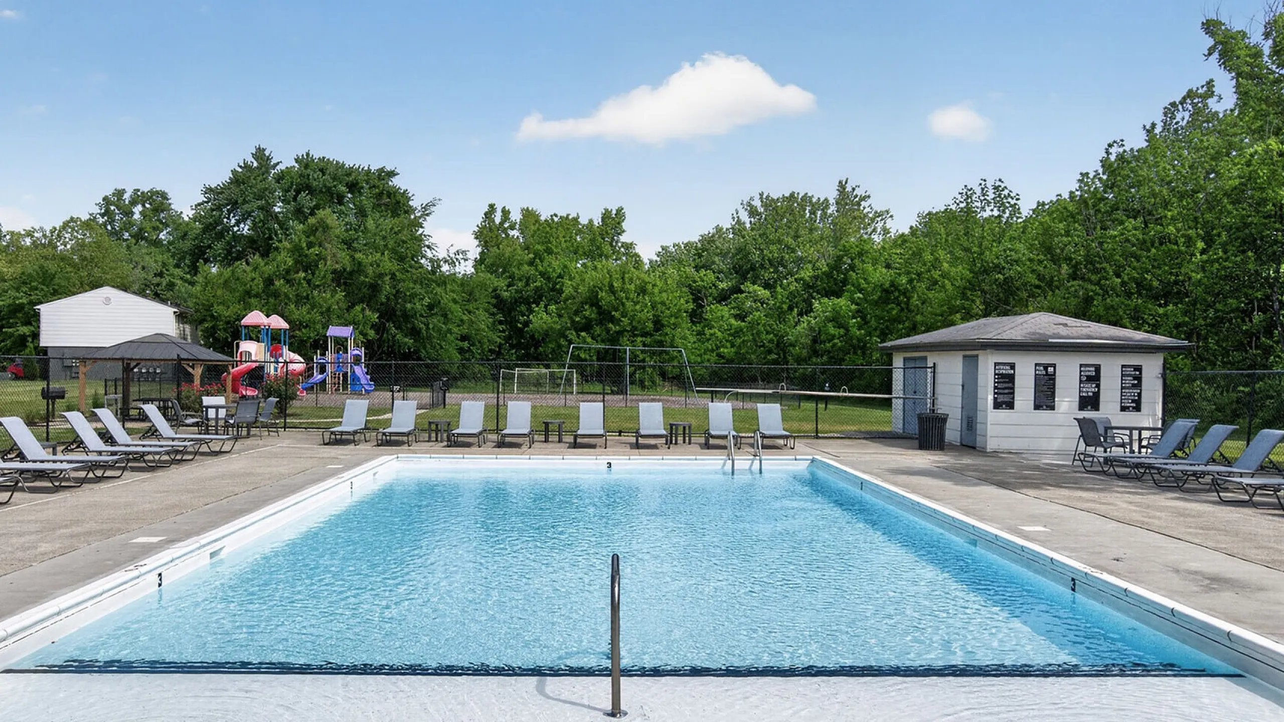 Inviting outdoor pool area with sun loungers, adjacent to a lush green playground, offering a perfect family-friendly retreat.