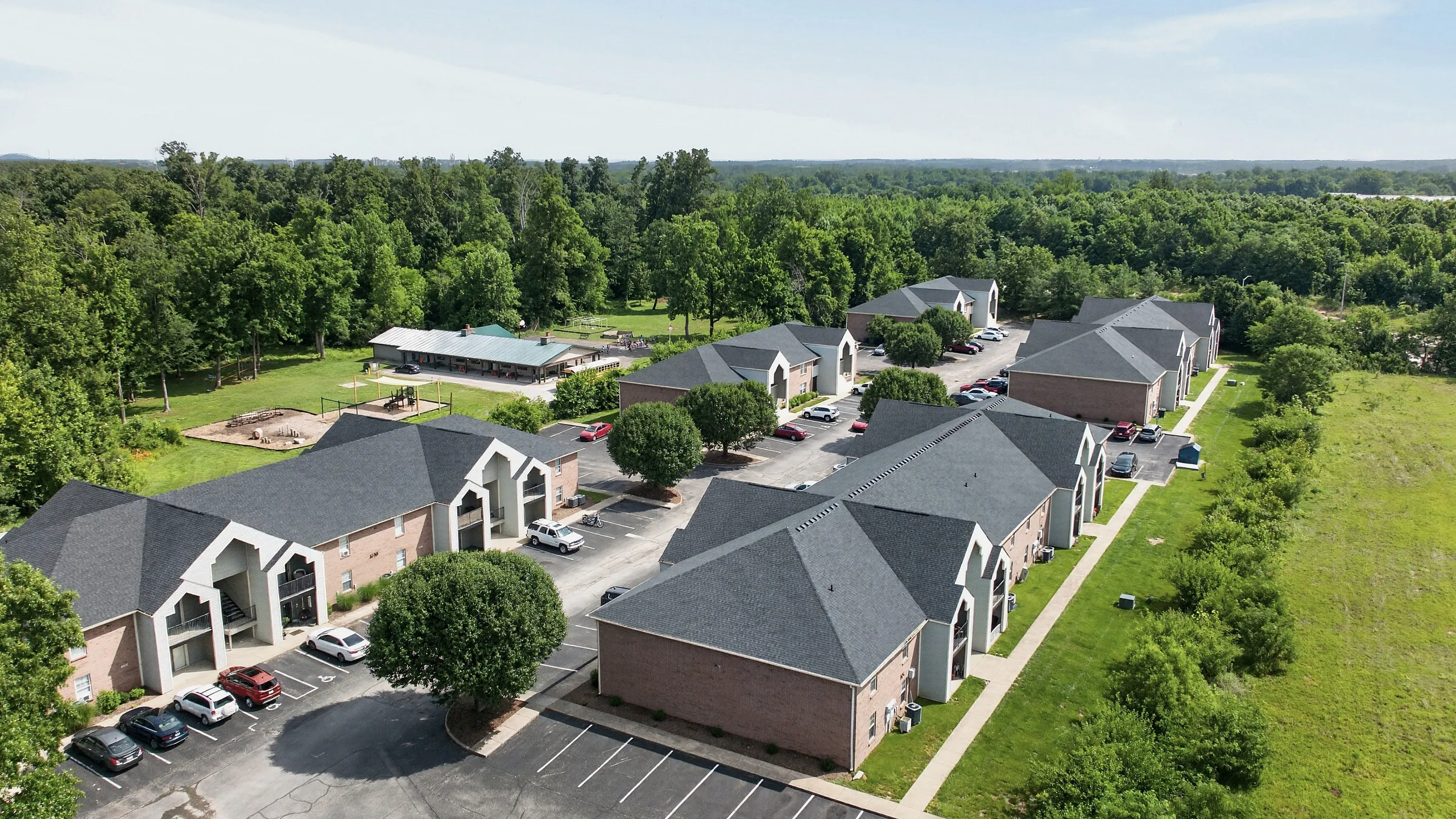Charming aerial view of modern apartments with lush green surroundings and ample parking, offering a serene living experience.
