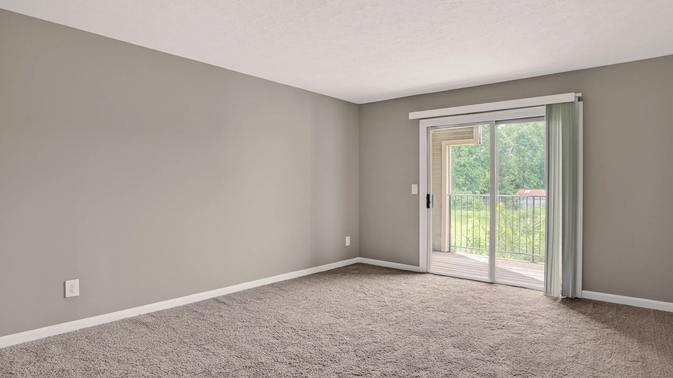 Bright, spacious room with plush carpet and large sliding glass doors leading to a serene balcony view.