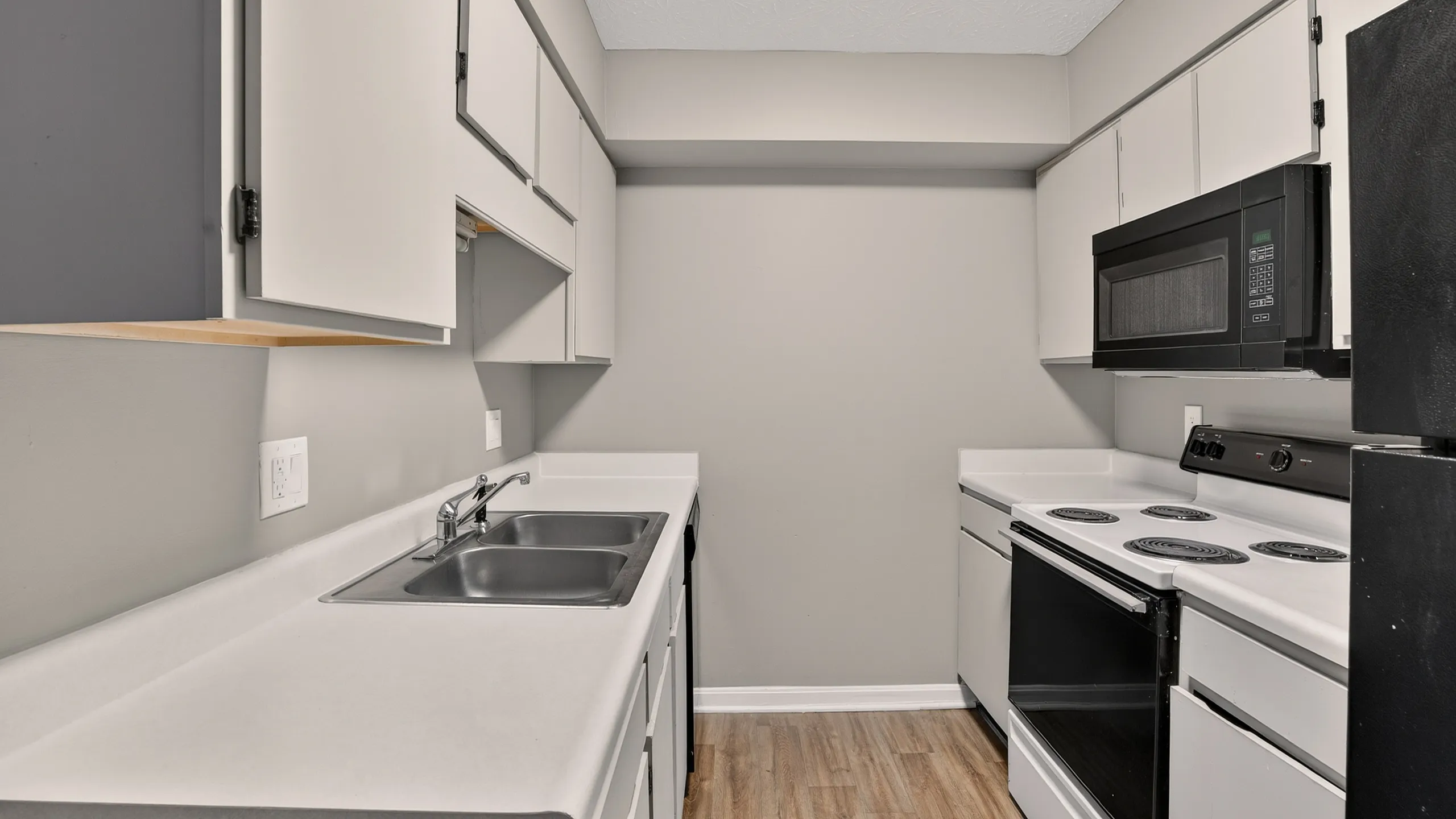 Chic modern kitchen with sleek white cabinetry, double sink, and efficient appliances, set on elegant wood flooring.