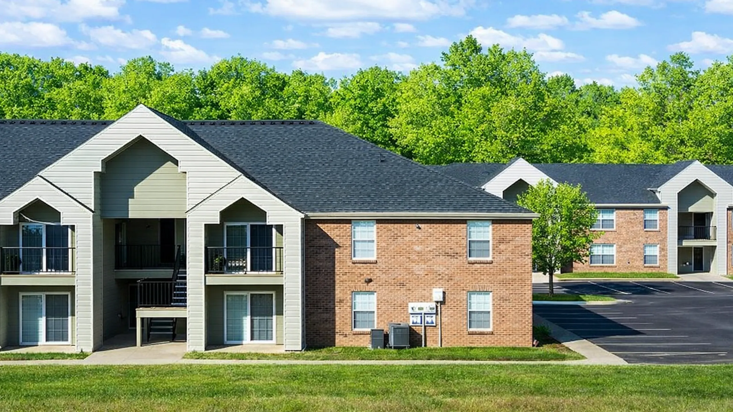 Charming apartment complex with brick facades, nestled in lush greenery, featuring modern balconies and ample parking.