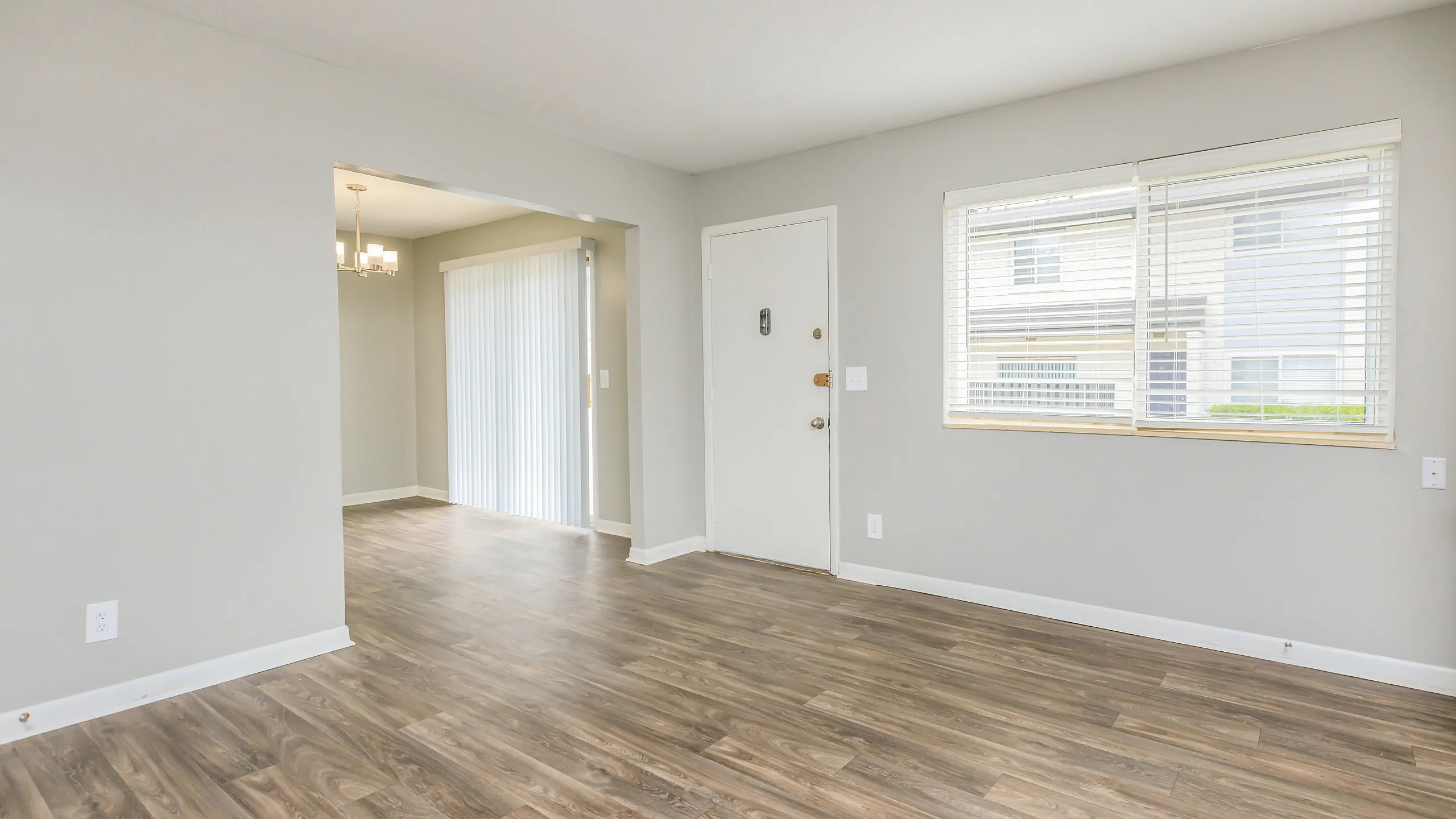 Inviting living area with elegant wood flooring, large sunlit window, and chic chandelier in dining space.
