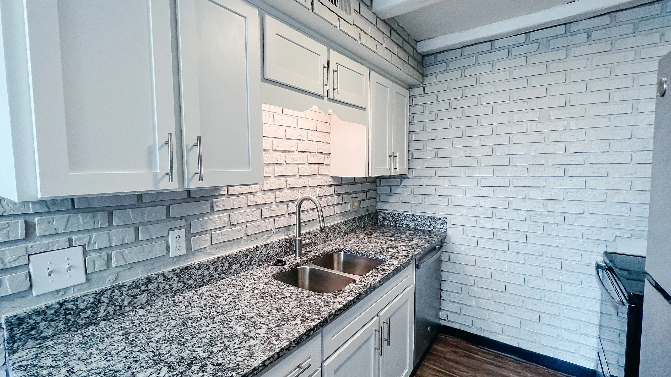 Modern kitchen with elegant granite countertops, sleek white cabinets, and stylish exposed brick walls.