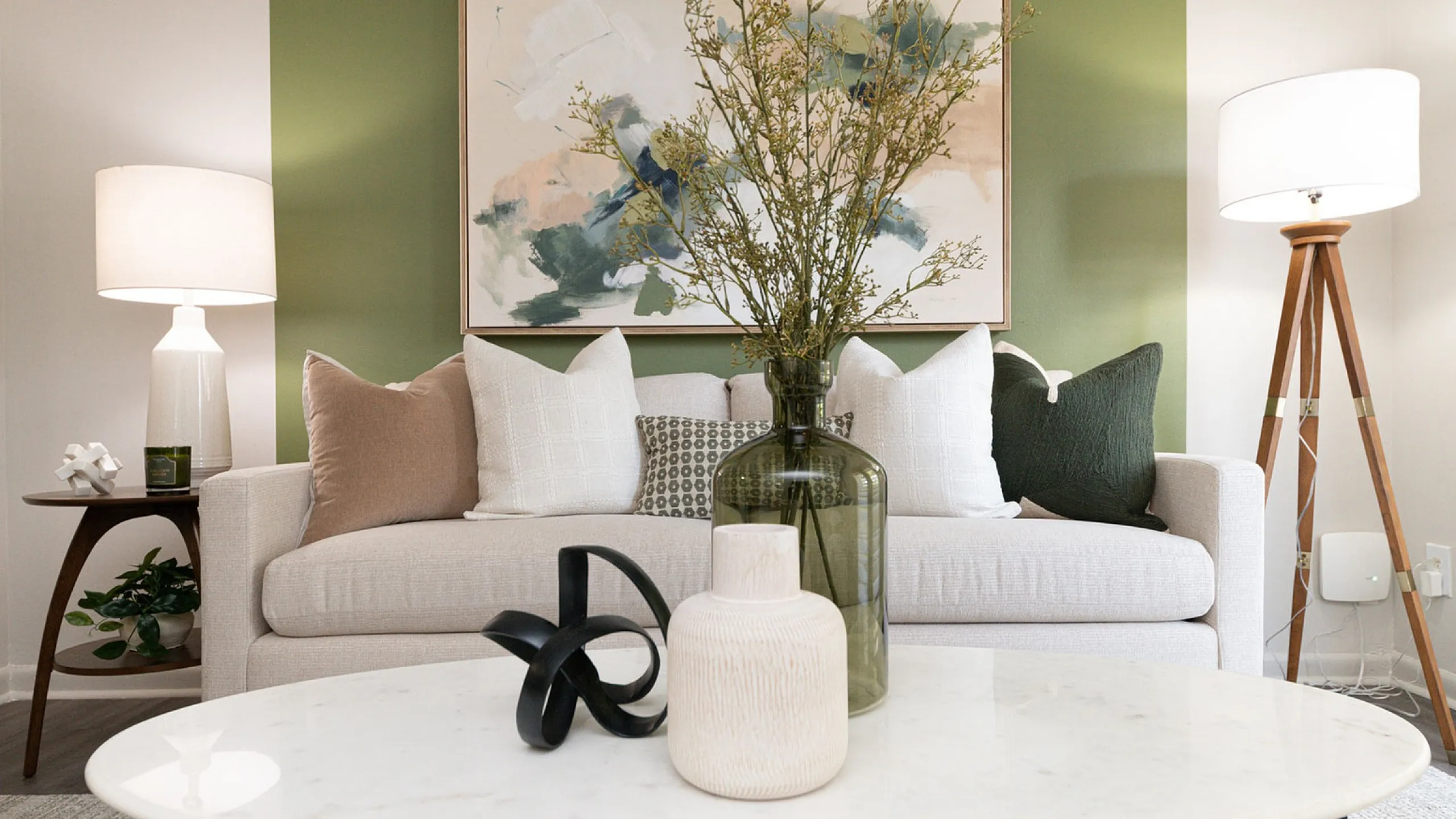 Elegant living room with modern decor featuring a cozy sofa, abstract wall art, and chic lighting on a stylish green accent wall.