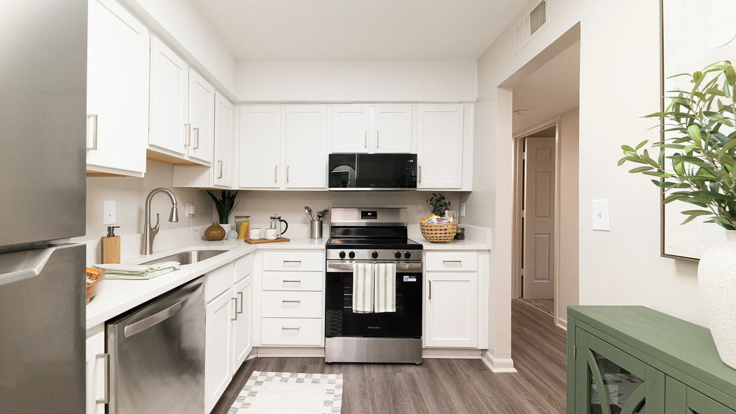 Modern kitchen featuring sleek white cabinets, stainless steel appliances, and elegant wooden flooring, perfect for culinary enthusiasts.