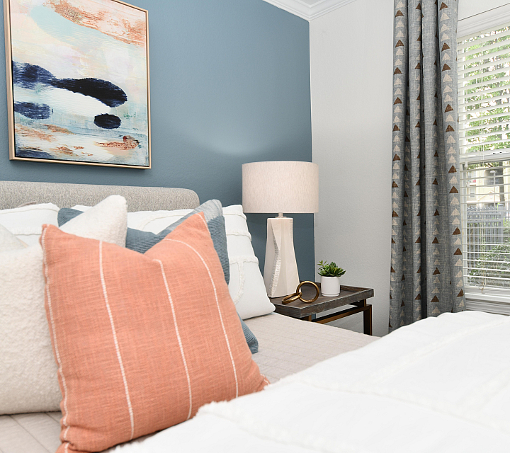 Inviting bedroom with elegant decor, featuring a soft bed, vibrant pillows, abstract wall art, and a sunlit window with stylish curtains.
