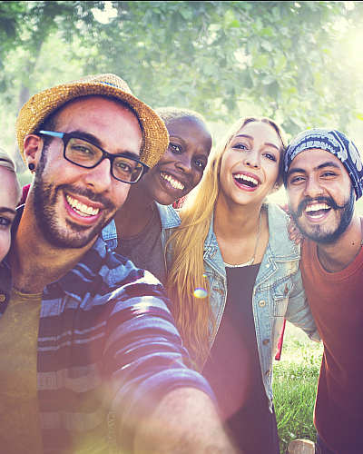Vibrant group of friends smiling outdoors in a lush, sunny park setting.