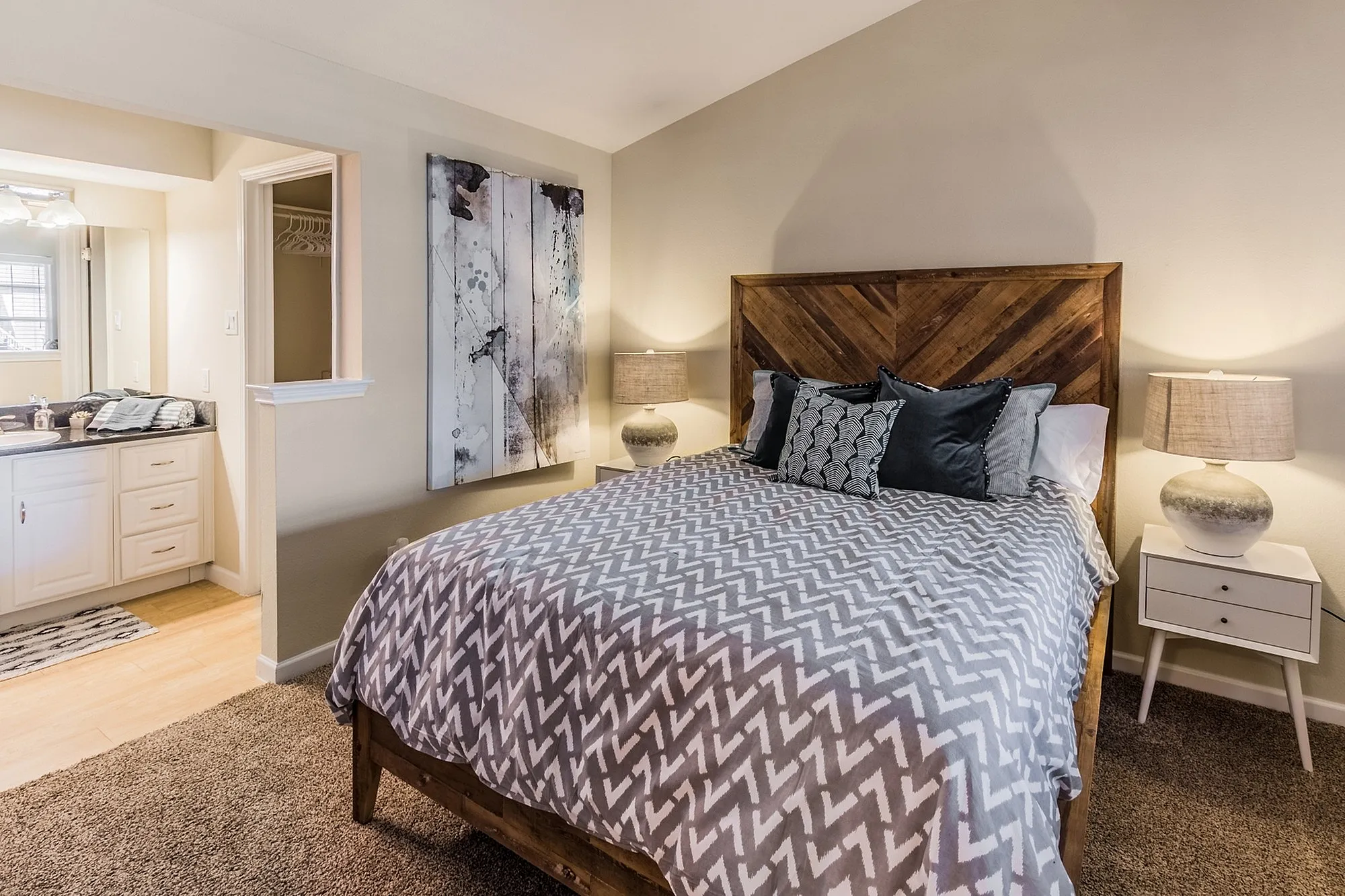 Cozy bedroom with stylish wooden headboard, soft lighting from modern lamps, and abstract wall art, featuring a plush bed with patterned bedding.