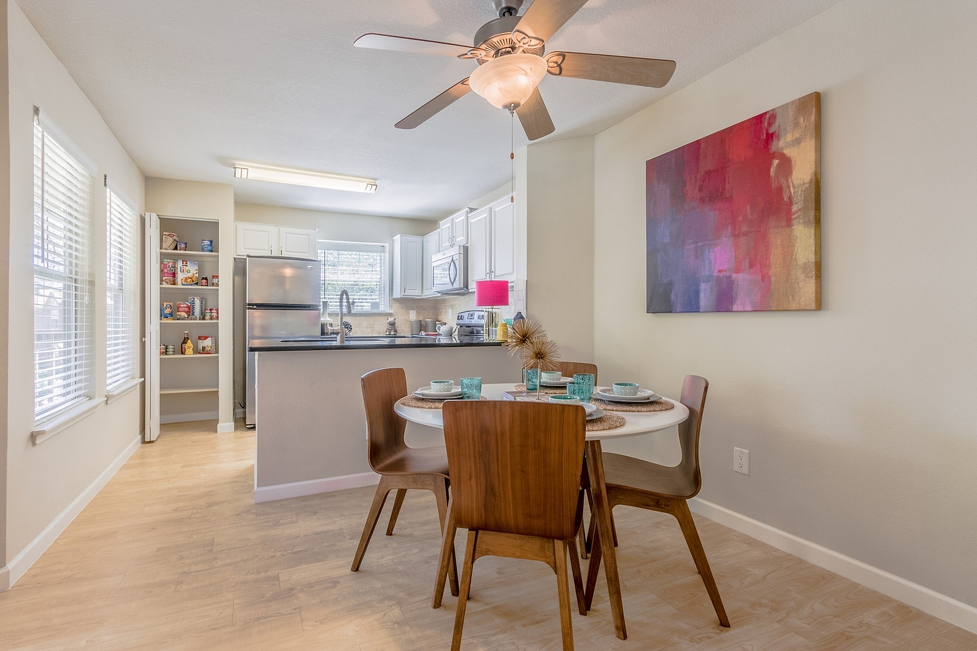 Bright and inviting dining area with modern wooden chairs and a cozy kitchen featuring elegant white cabinets and sleek stainless steel appliances.