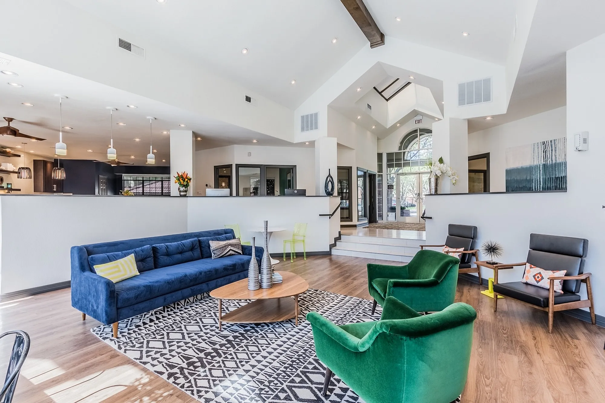 Luxurious open-concept living room featuring a modern blue sofa, vibrant green armchairs, and stylish decor, illuminated by chic pendant lighting and large windows.