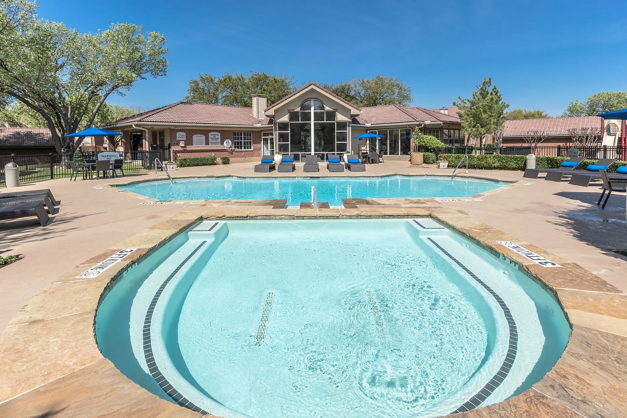 Luxurious apartment complex pool area with inviting lounge chairs, surrounded by lush landscaping and a charming clubhouse.