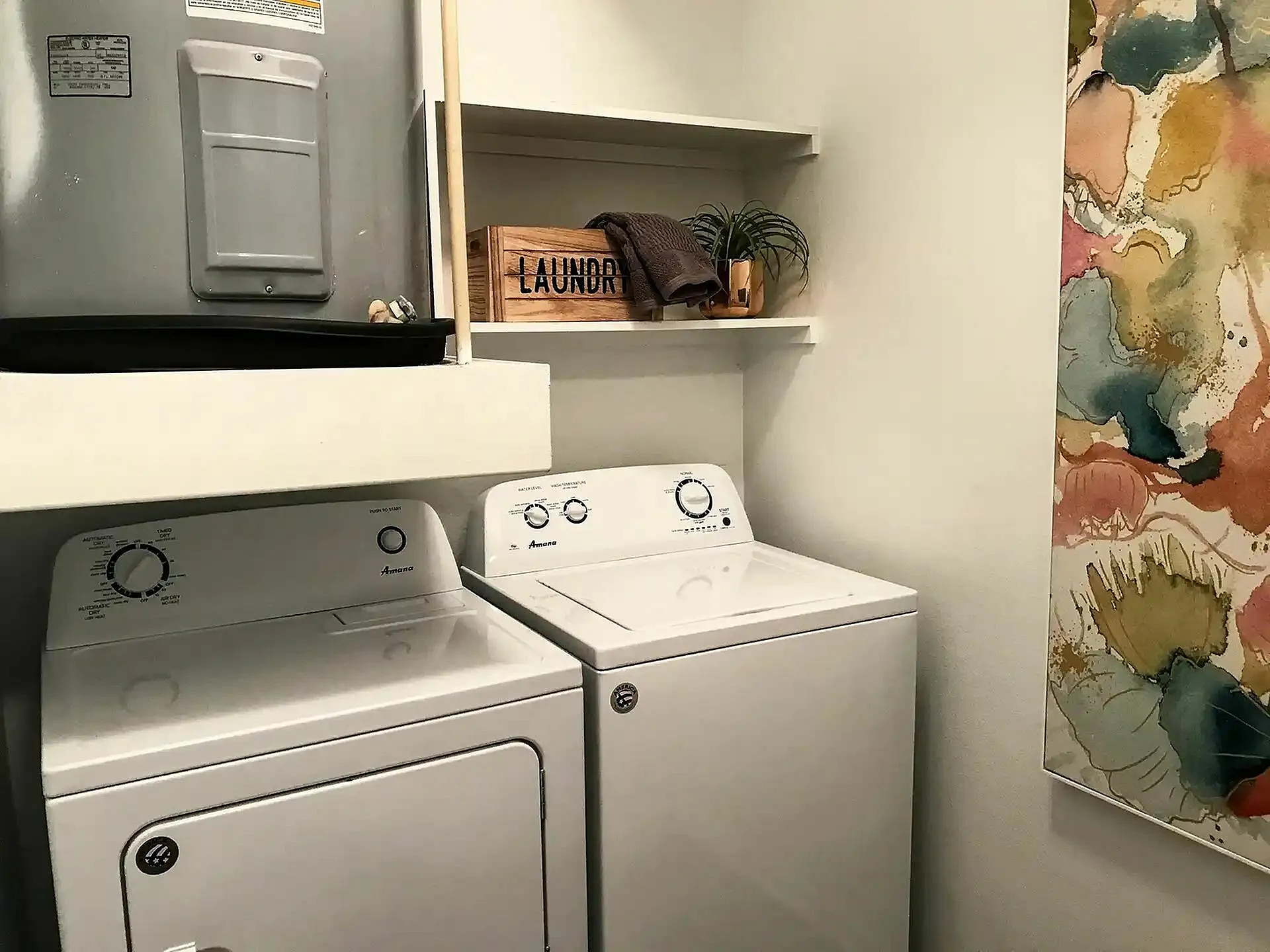 Chic laundry room with modern washer and dryer, vibrant abstract artwork, and stylish shelving.