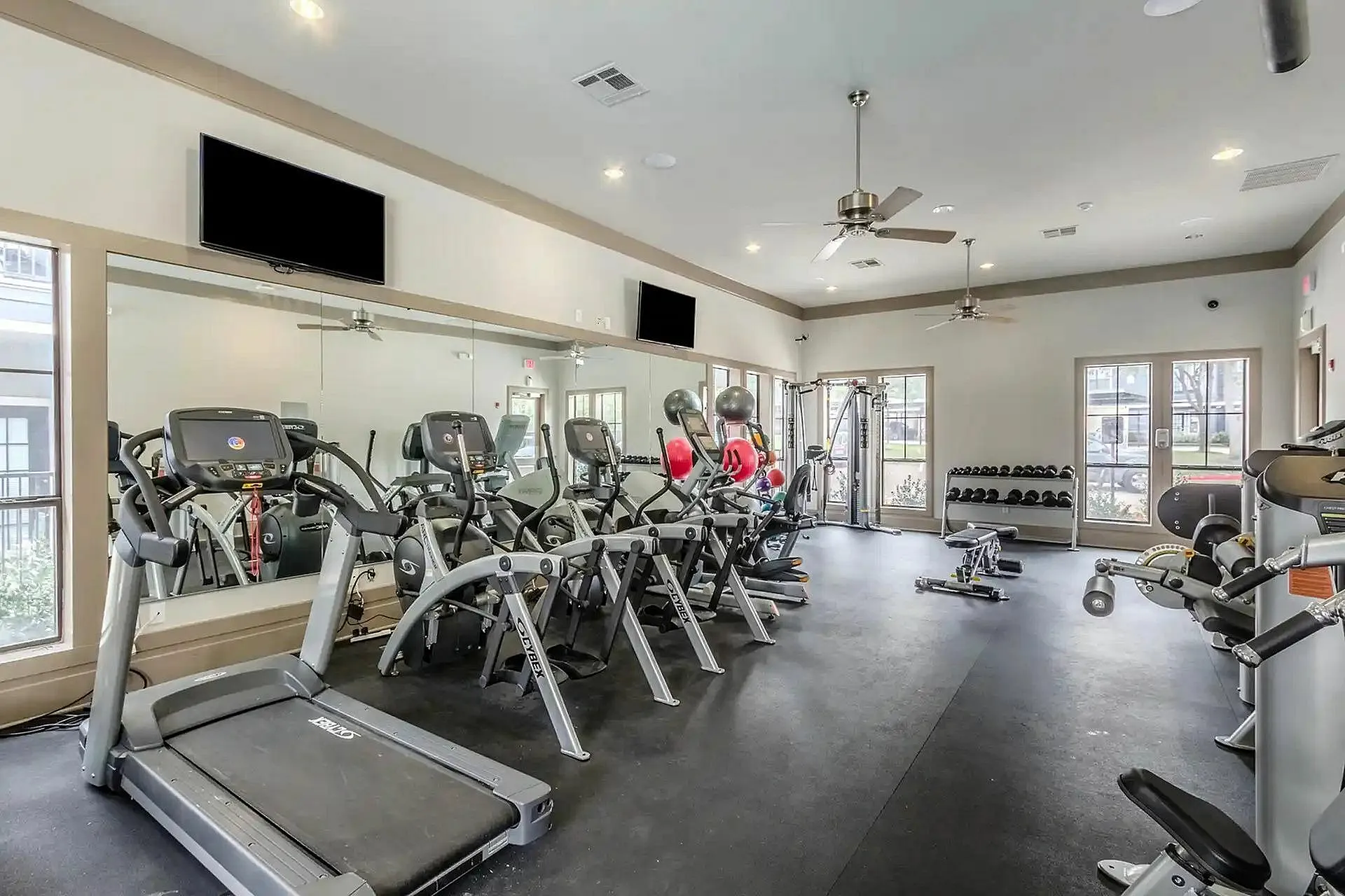 Modern fitness center with state-of-the-art exercise machines, free weights, natural light, and wall mirrors.