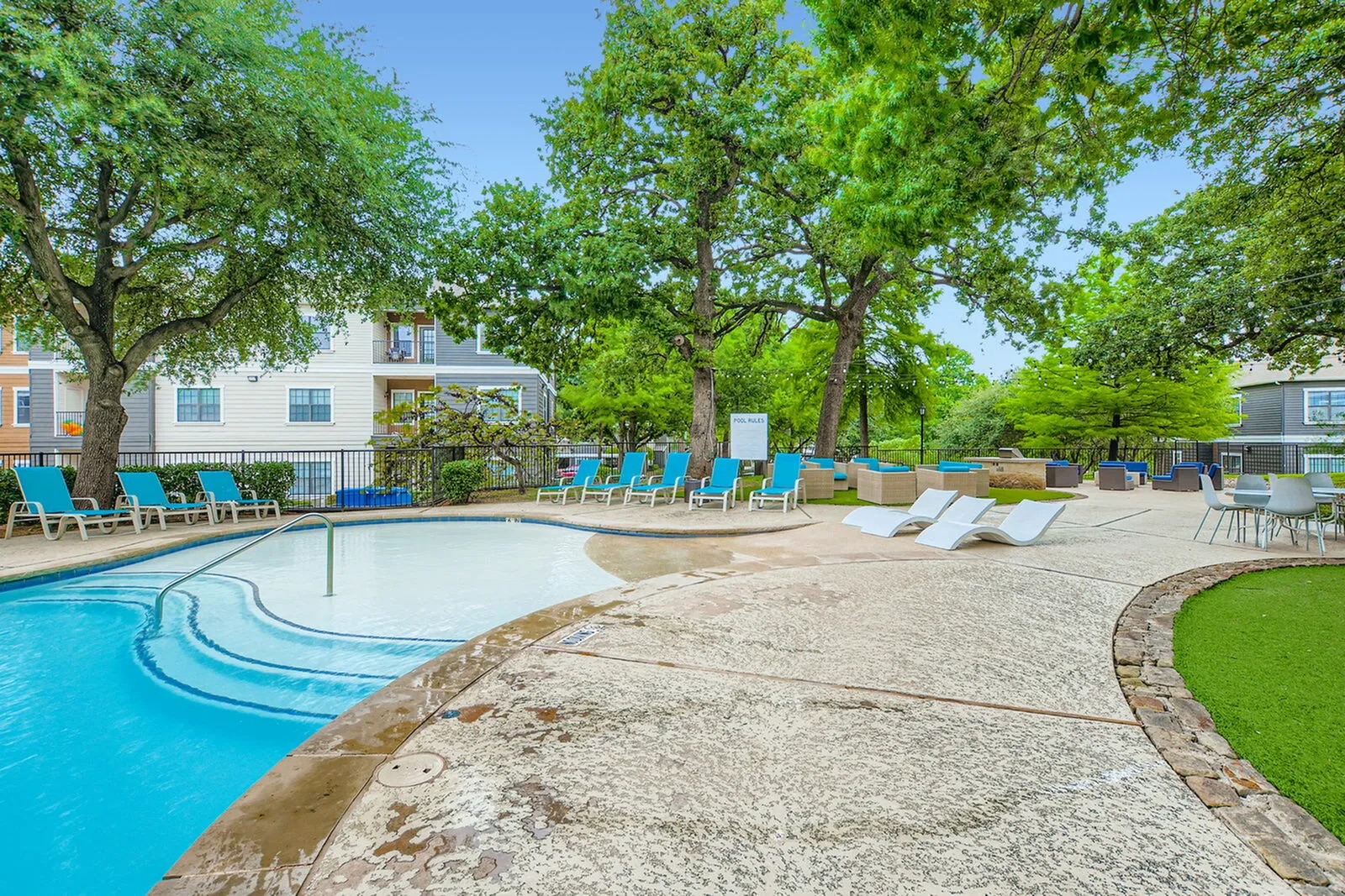 Luxurious apartment pool area with relaxing lounge chairs, surrounded by lush greenery and modern apartments.