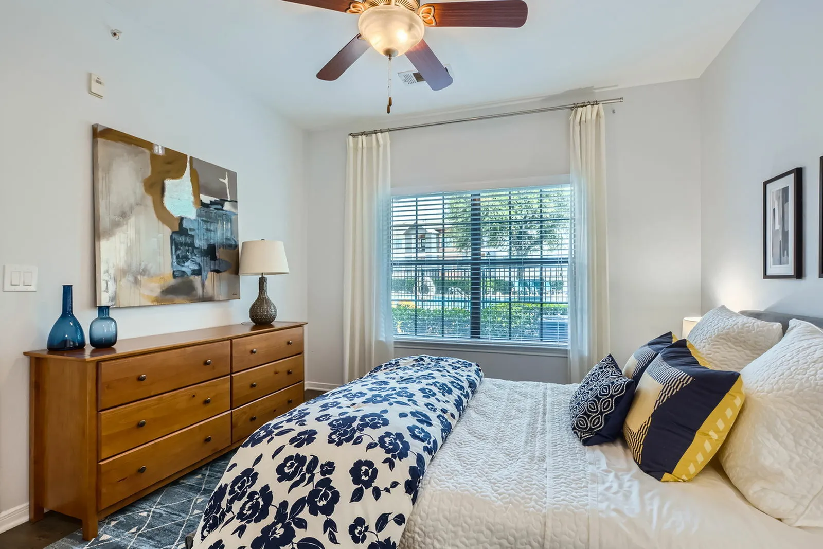 Charming bedroom with a cozy bed, stylish floral comforter, elegant wooden dresser, and large window offering plenty of natural light.