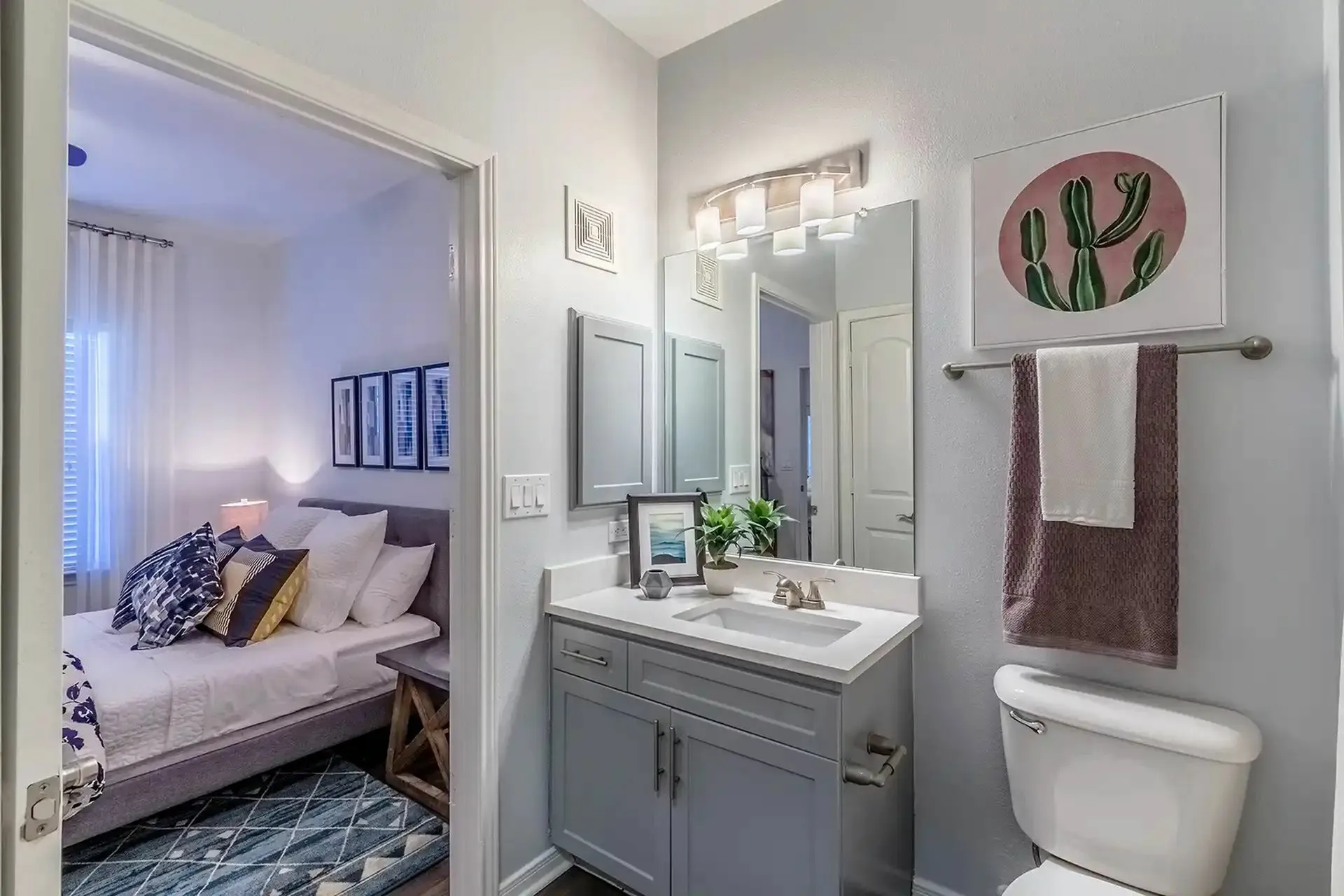 Modern apartment bathroom with a sleek vanity, artistic decor, and glimpse of a cozy, well-lit bedroom.